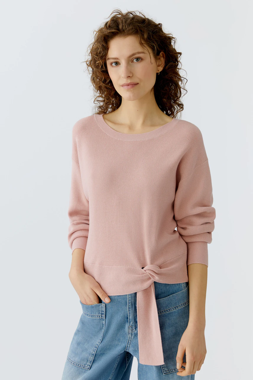 Casual women's pullover: Young woman in a light pink pullover with a knot detail, paired with denim.