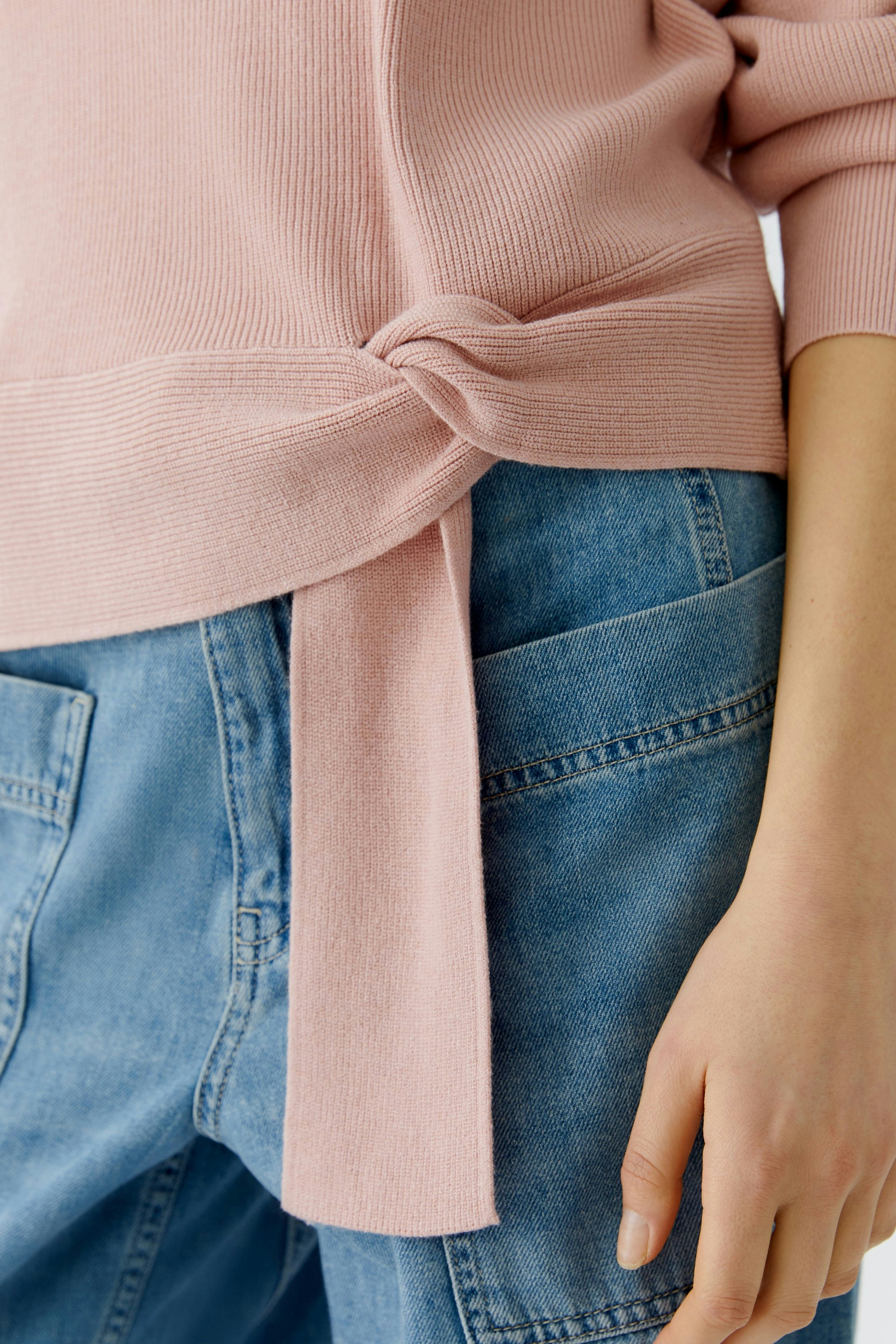Casual women's pullover: Close-up of a pink pullover with a knot detail, paired with denim.