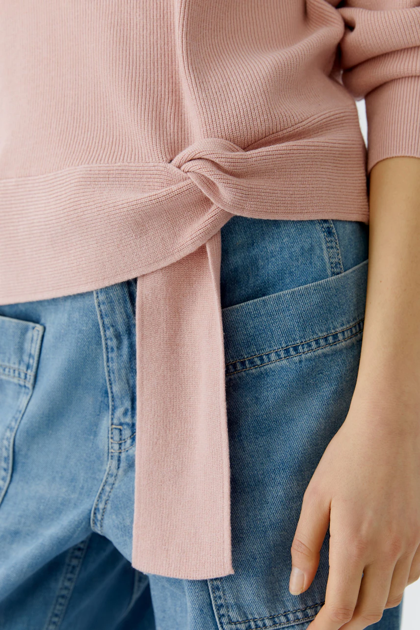 Casual women's pullover: Close-up of a pink pullover with a knot detail, paired with denim.