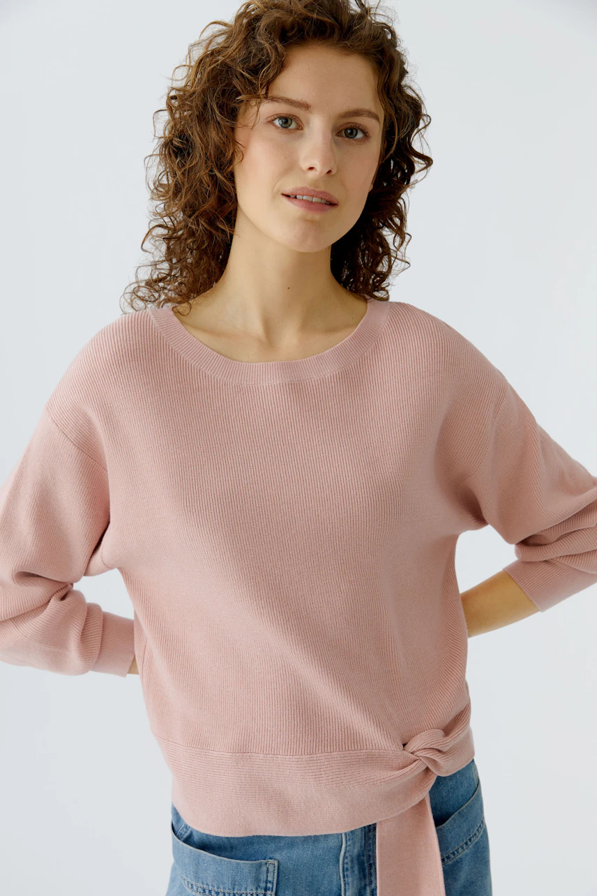 Casual women's pullover: Young woman in a pink pullover with a knotted detail, paired with denim.