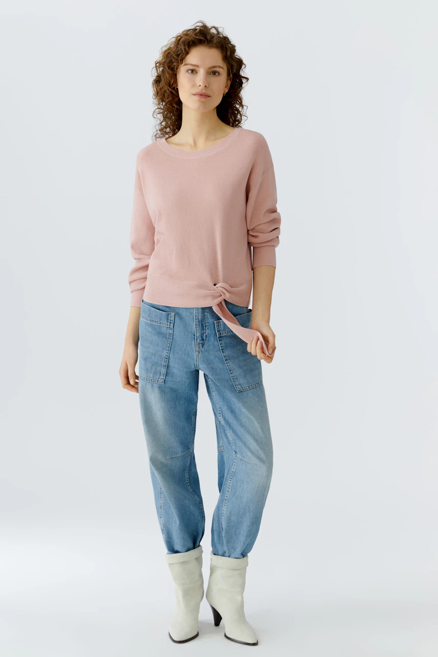 Casual women's pullover: A woman in a light pink pullover with a knotted detail, paired with relaxed jeans.