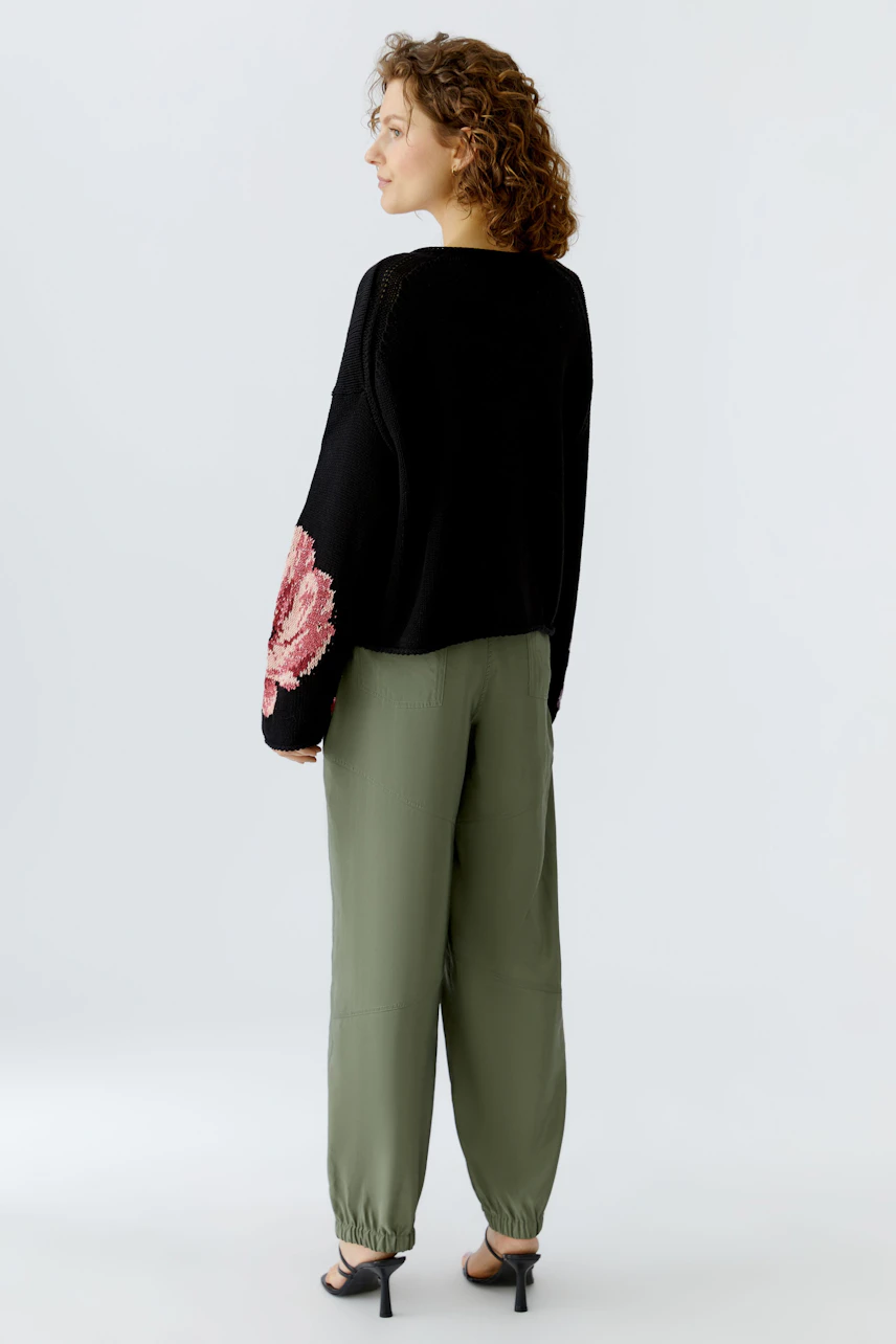 Damen-Pullover: Frau in schwarzem Pullover mit floralem Muster und lässigen Hosen von hinten.