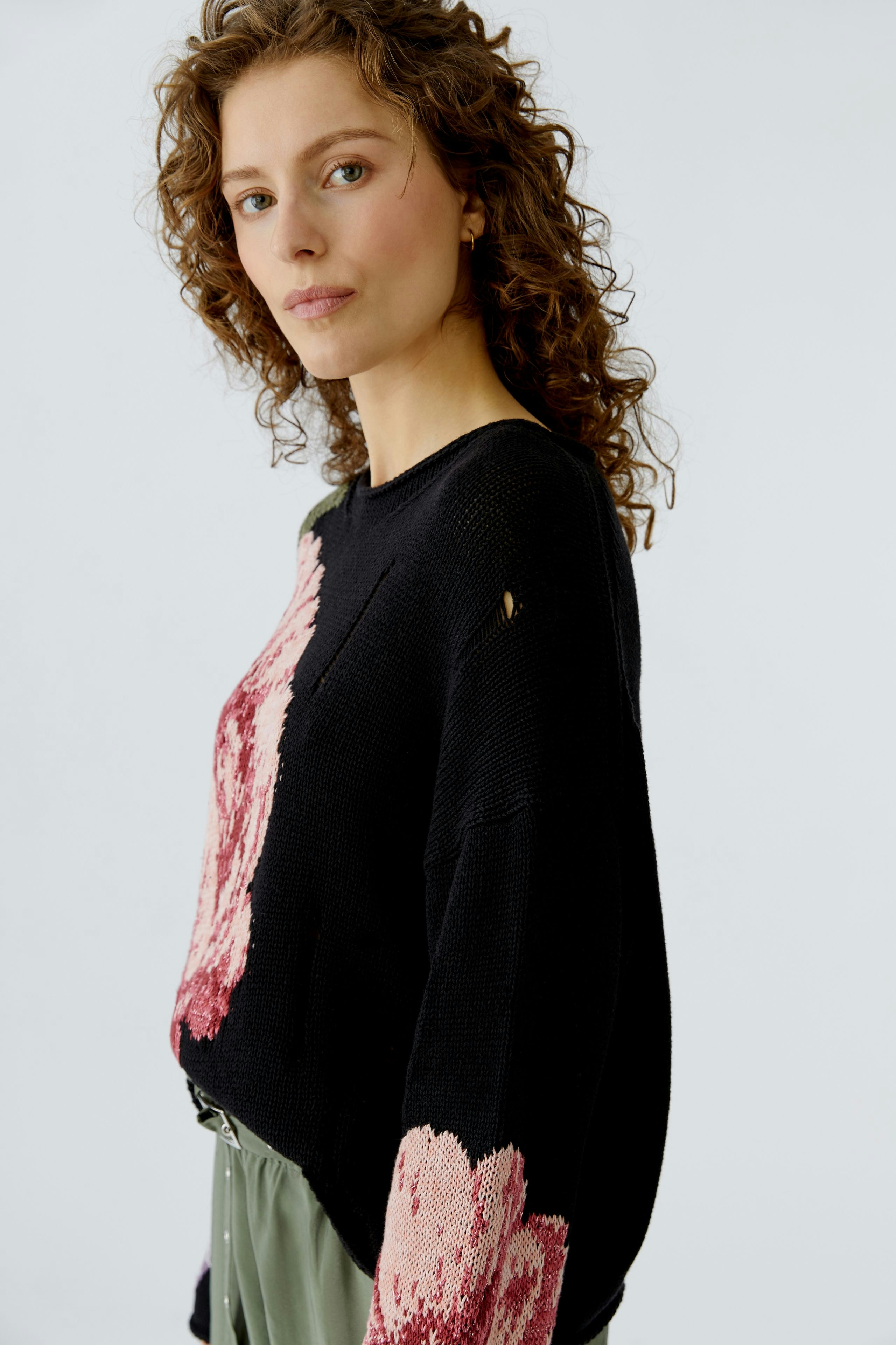 Casual women's pullover: A woman in a black pullover with pink floral patterns, styled with relaxed trousers.