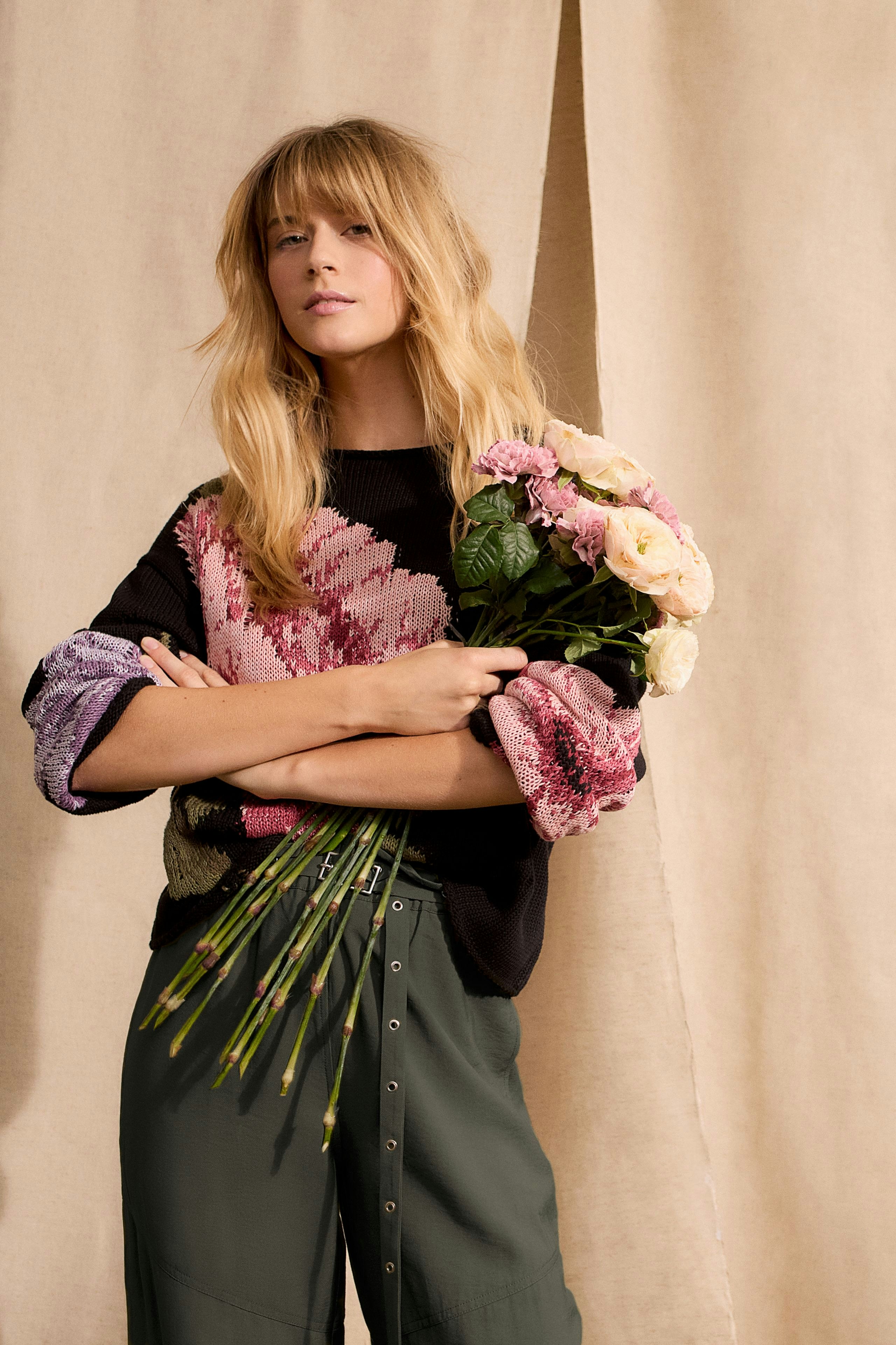 Modern women's pullover: Woman in a colorful knit pullover holding flowers, exuding a relaxed vibe.
