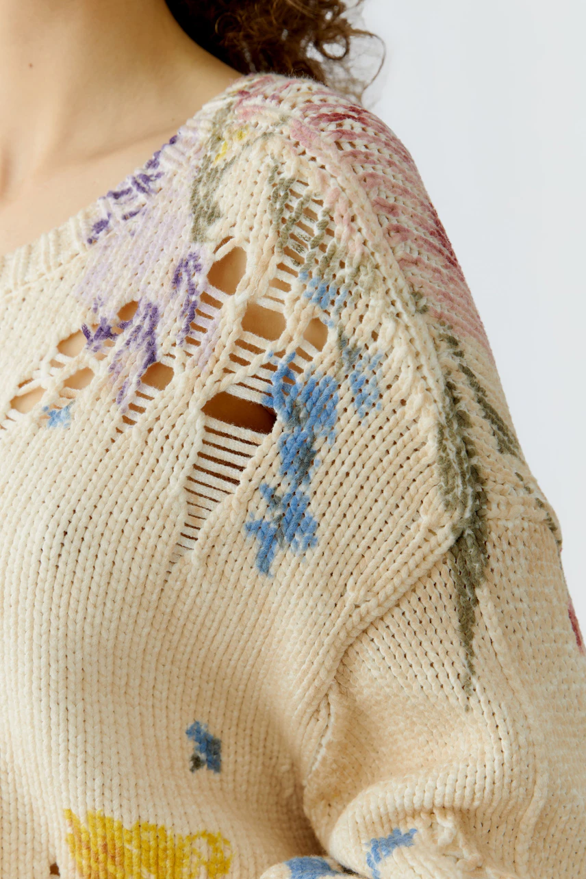 Casual women's pullover: Close-up of a woman in a light, floral-patterned knit pullover with distressed details.