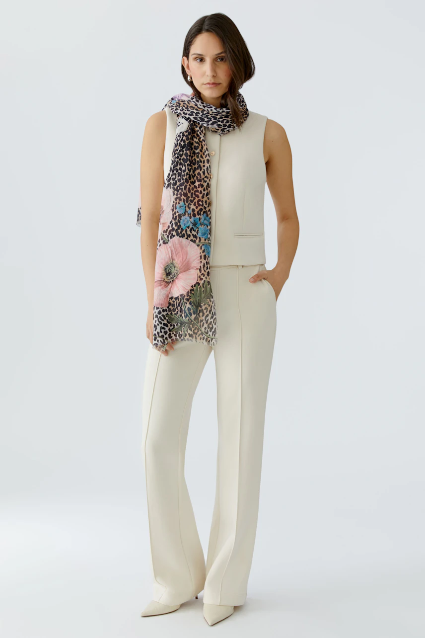 Damen-Schal: Frau trägt einen bunten Schal mit Blumen- und Tiermuster, kombiniert mit einem hellen Outfit.