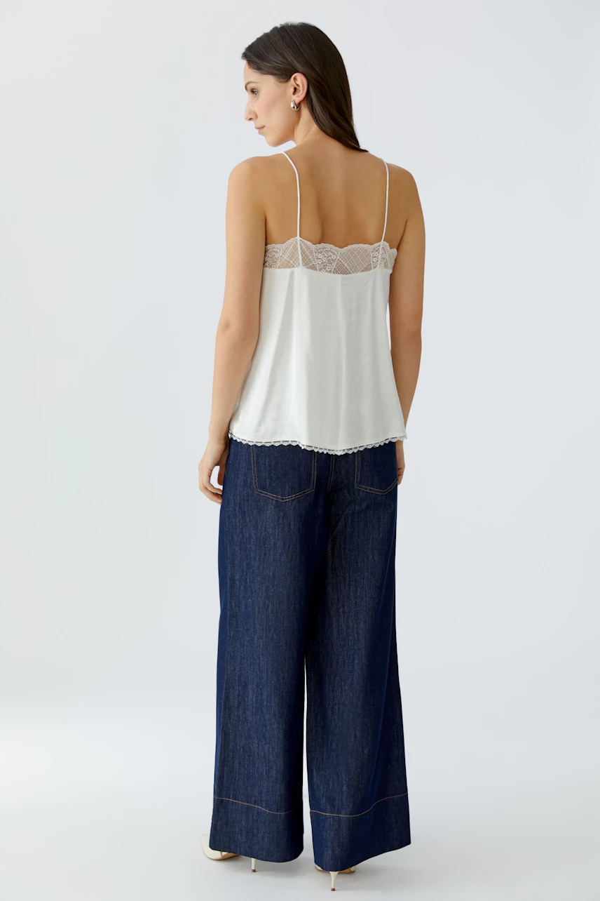 Damen-Top: Frau trägt ein weißes Spaghetti-Top mit Spitzenbesatz und lässigen Jeans.