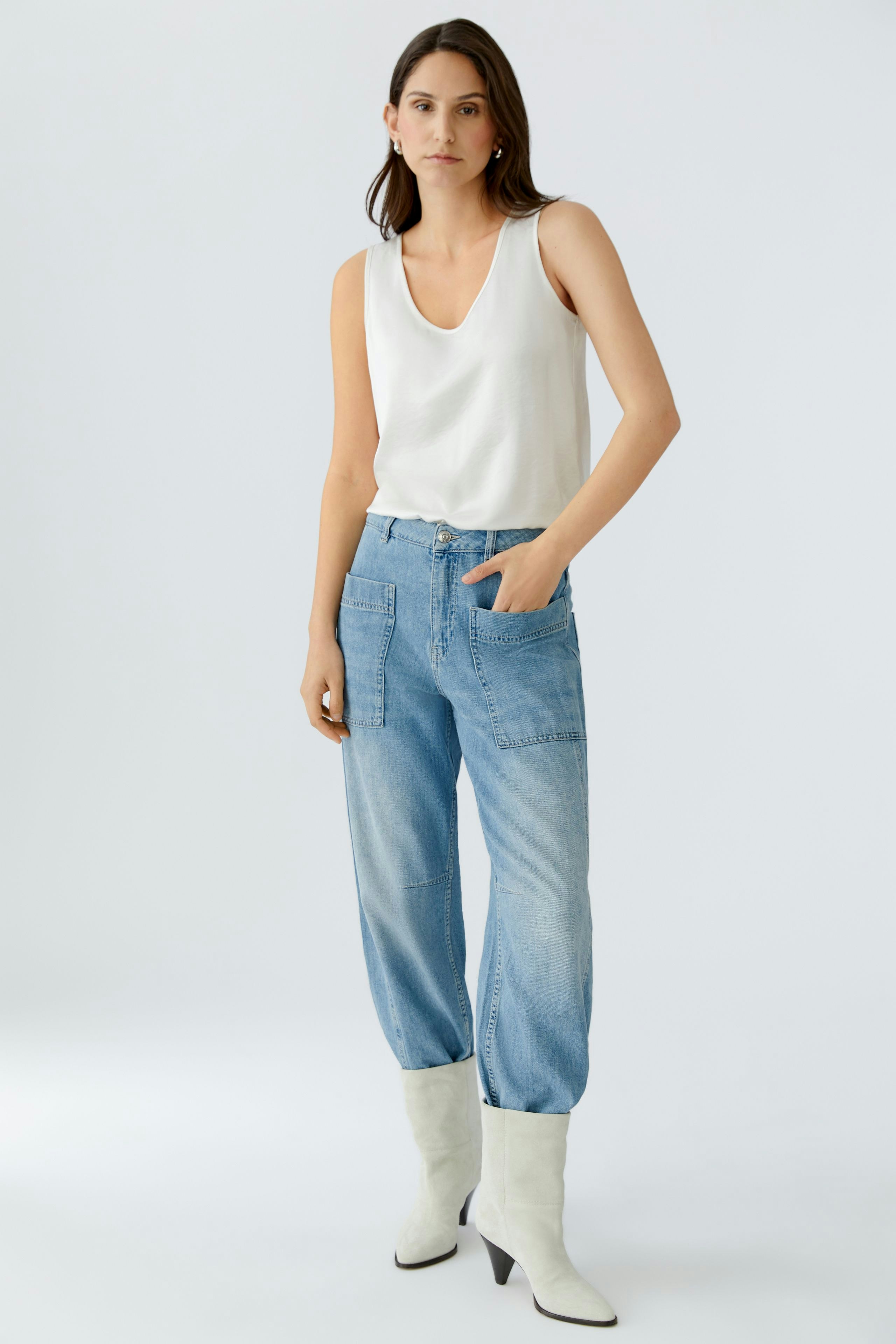 Casual women's top: A woman in a white sleeveless top paired with relaxed-fit jeans.