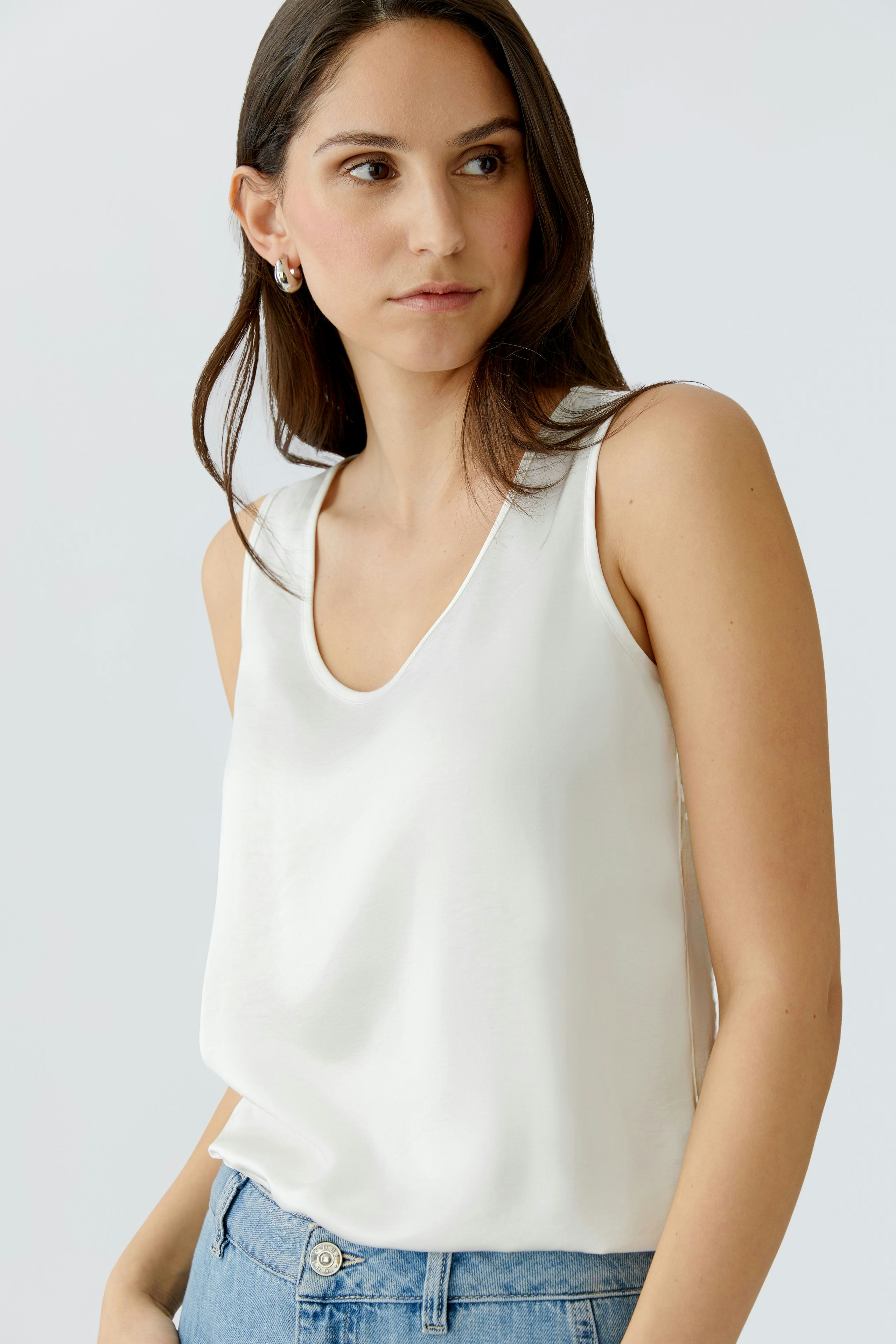 Casual women's top: Young woman in a white sleeveless top paired with denim shorts.