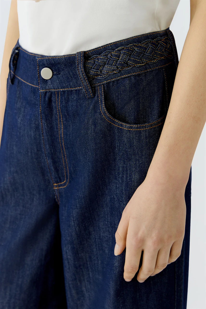 Wide leg jeans: Woman wearing dark blue jeans with a braided waistband, showcasing a relaxed fit.