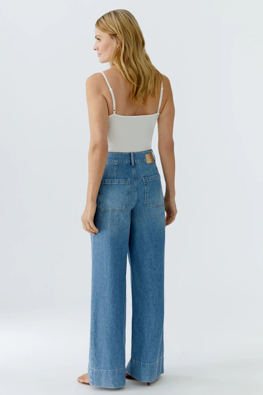 Damen Jeans Wide Leg: Frau in lässigen, weiten Jeans mit hohem Bund und praktischen Taschen.