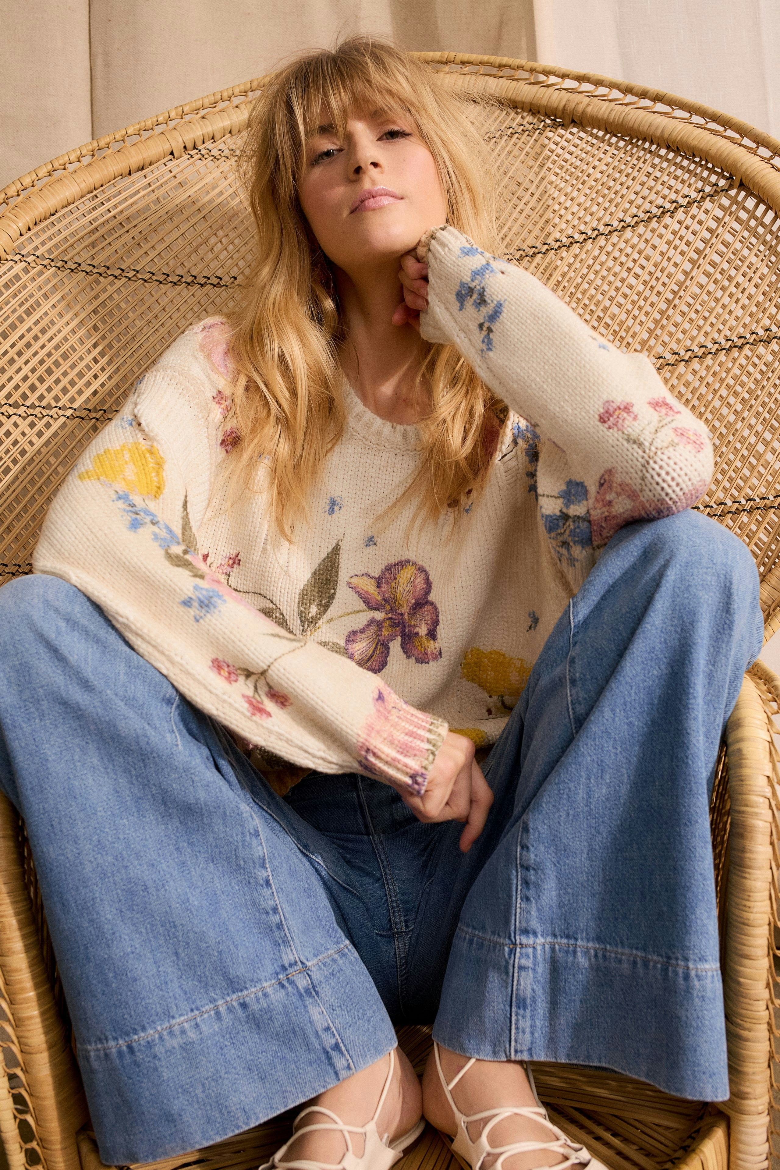 Wide leg jeans: A woman sits confidently in light blue wide leg jeans, paired with a floral pullover.