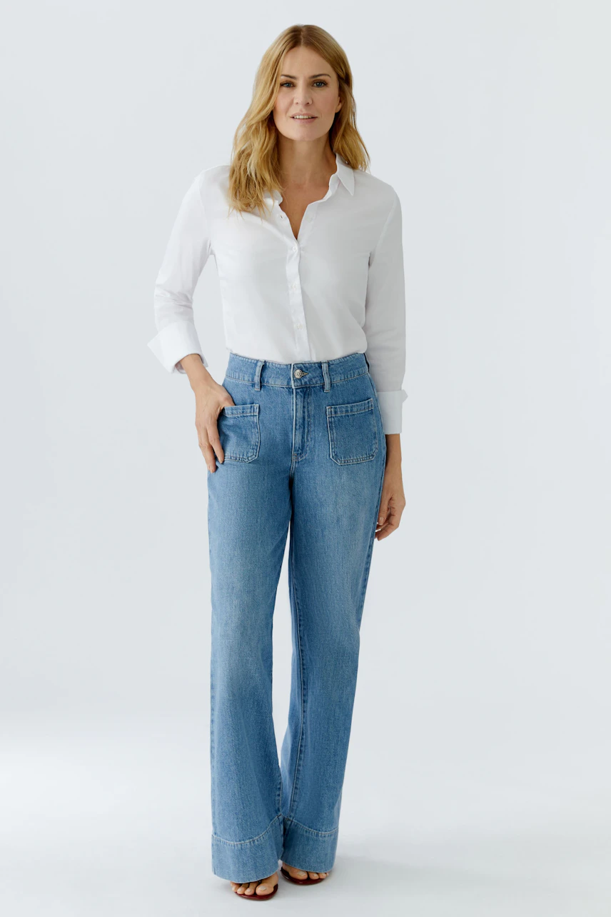 Damen Jeans Wide Leg: Frau in lässigen, weiten Jeans mit weißem Hemd und offenen Haaren.