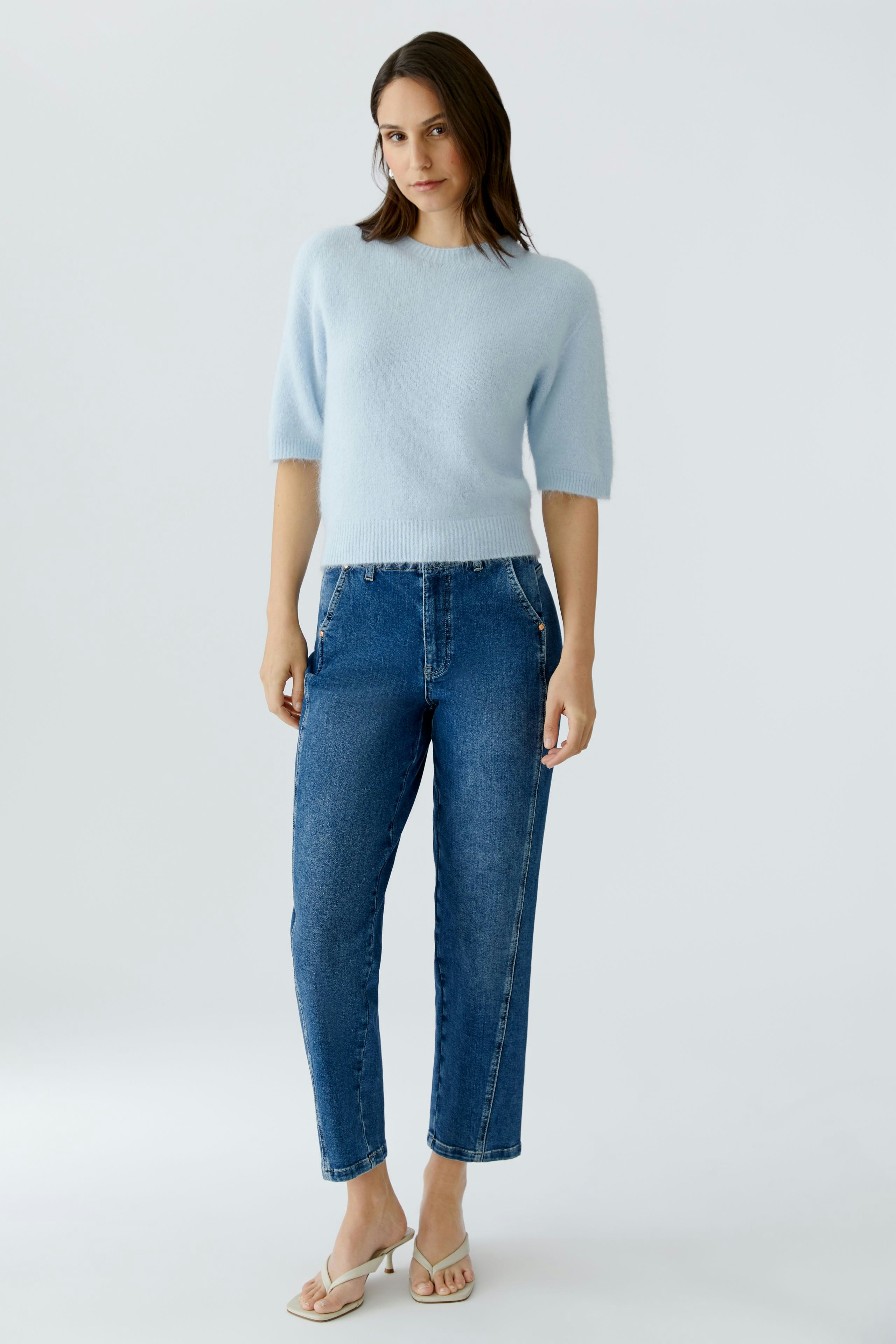 Tapered jeans: Woman in light blue top and tapered jeans stands confidently.