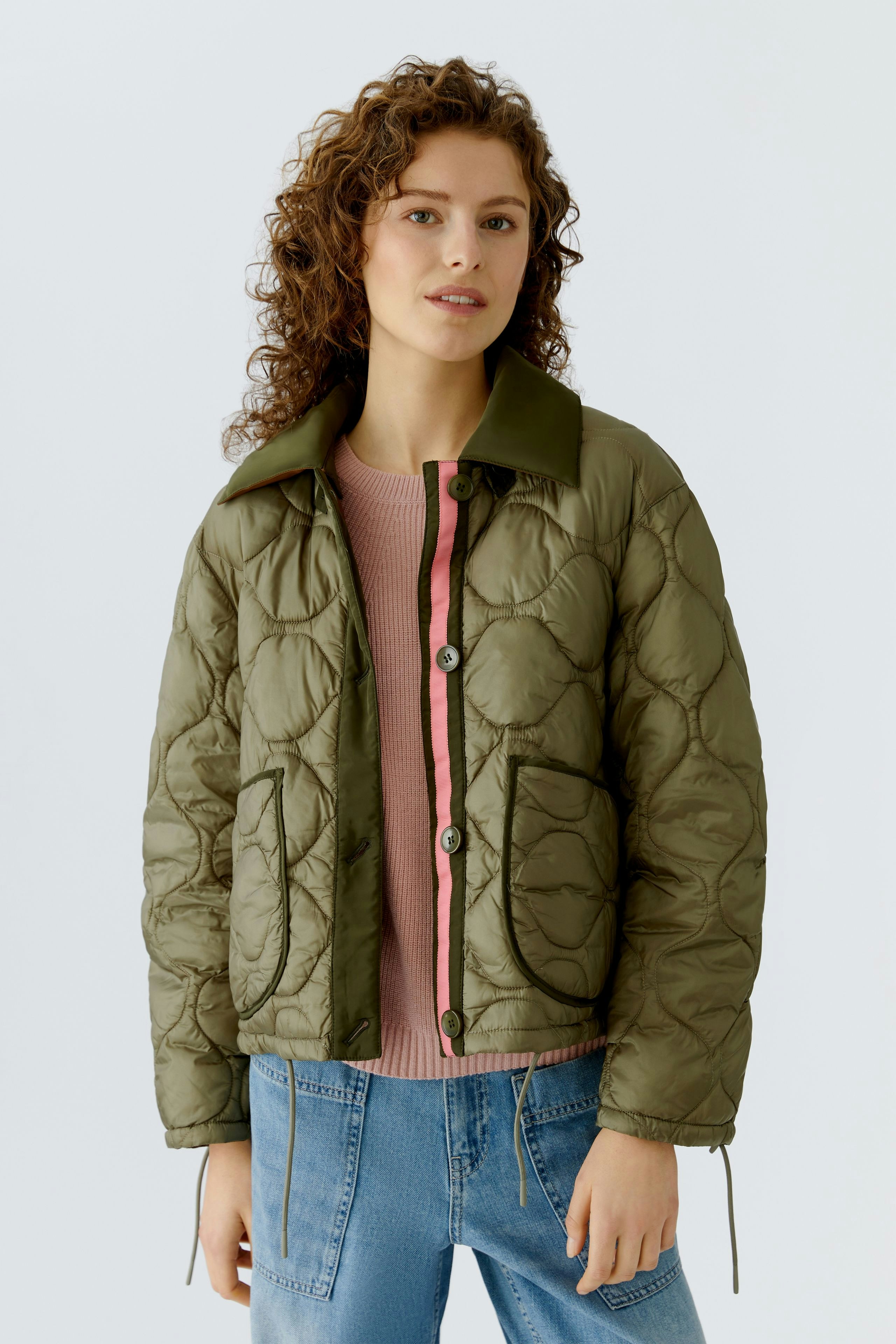 Reversible jacket: Woman in an olive green quilted jacket with a relaxed fit, paired with a pink pullover.