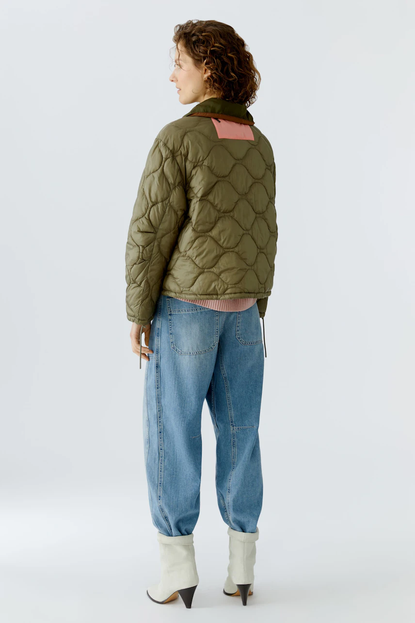 Wendejacke: Frau trägt eine olivgrüne, gesteppte Wendejacke mit pinkem Detail und lässigen Jeans.