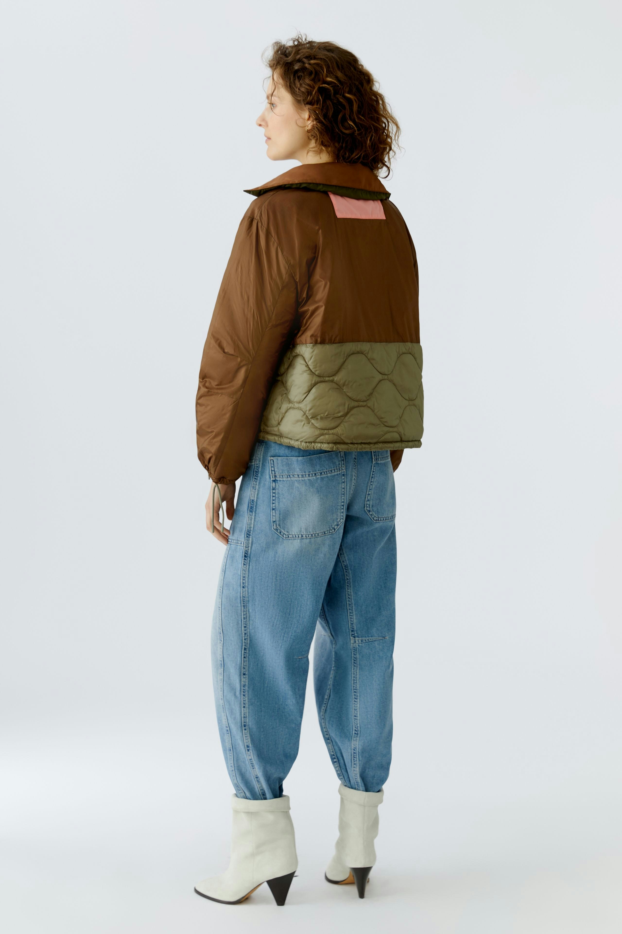 Reversible jacket: Woman in a brown and green puffer jacket, styled with relaxed blue jeans.