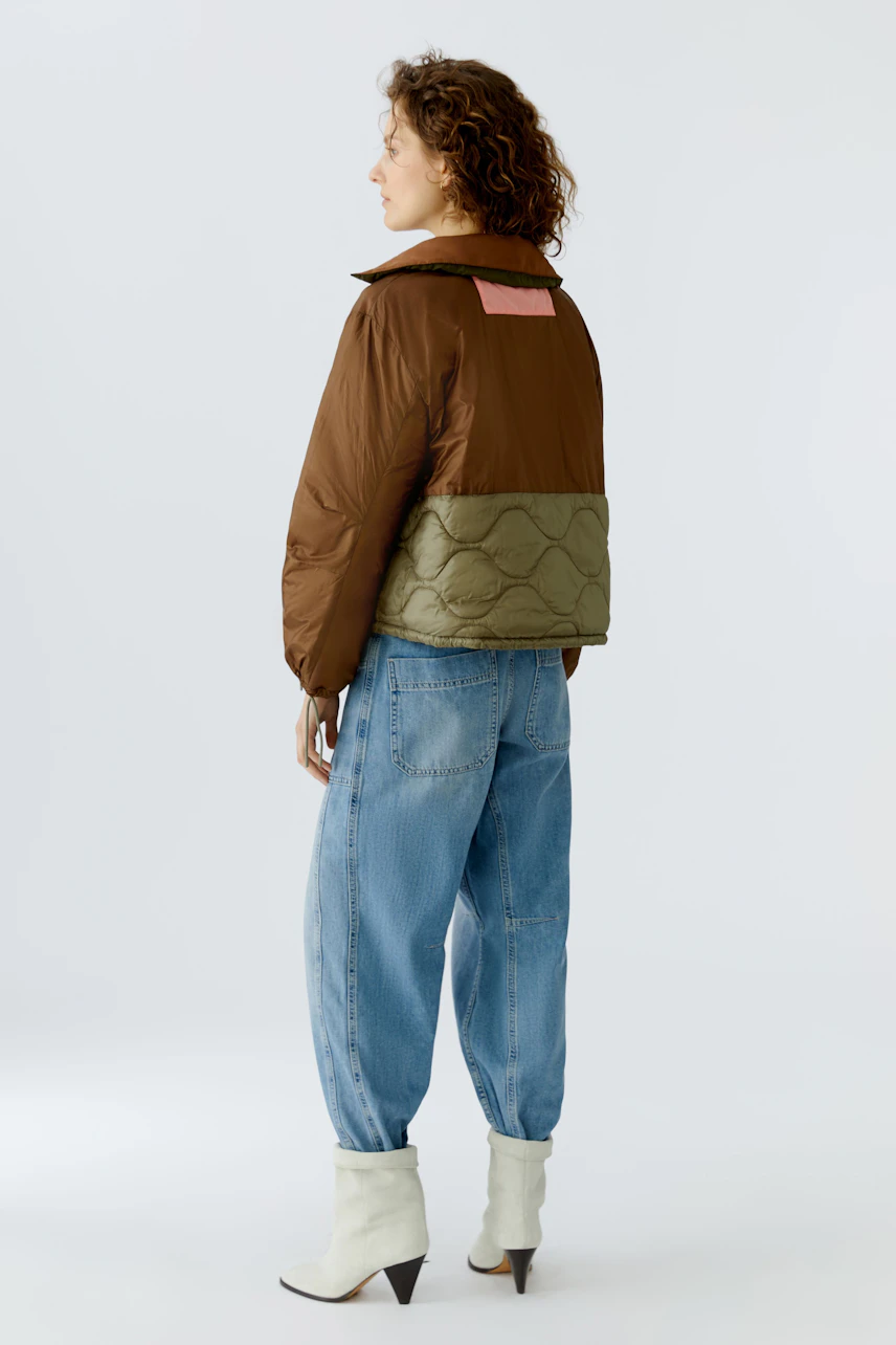 Wendejacke: Frau in brauner und olivgrüner Jacke mit lässigen Jeans und Stiefeln von hinten.