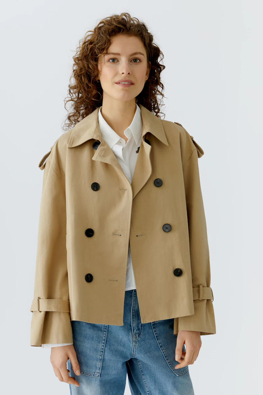 Beige Damen-Jacke: Frau trägt eine lässige, taillierte Jacke mit großen Knöpfen und breiten Ärmeln.