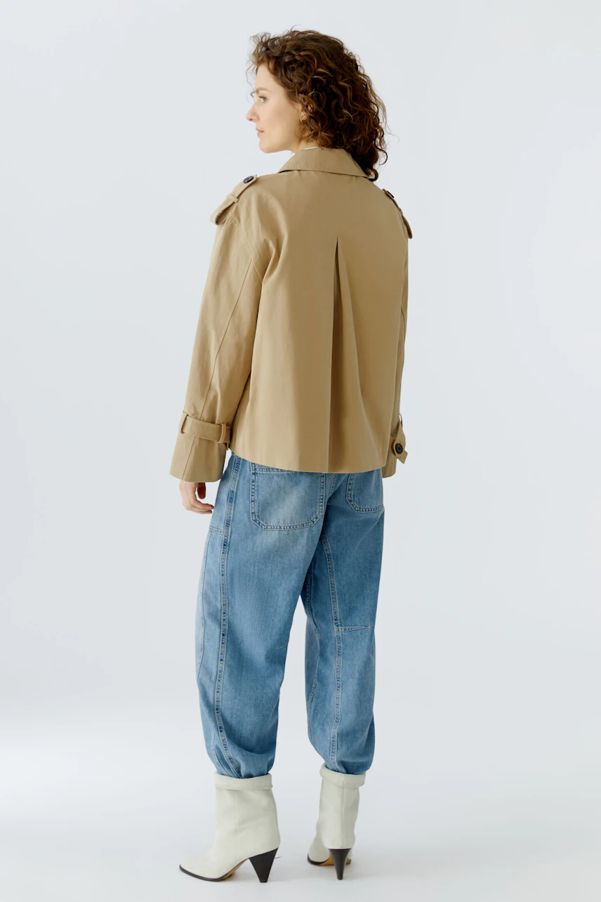 Bequeme Damen-Jacke: Frau mit lockigen Haaren trägt eine beige Jacke und lässige Jeans.