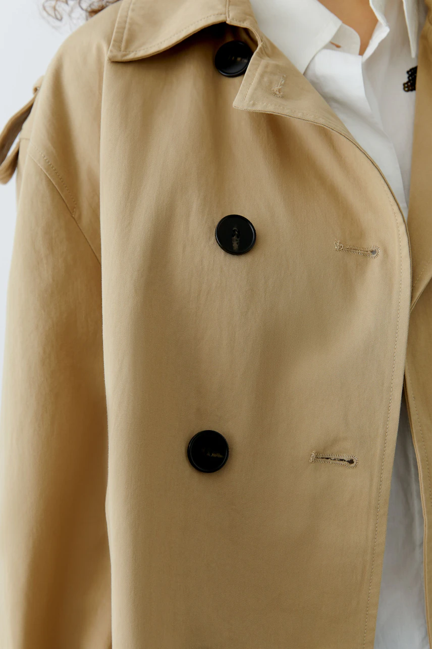 Beige Damen-Jacke: Frau trägt eine lässige, knöpfbare Jacke mit großen Knöpfen und einem modernen Schnitt.