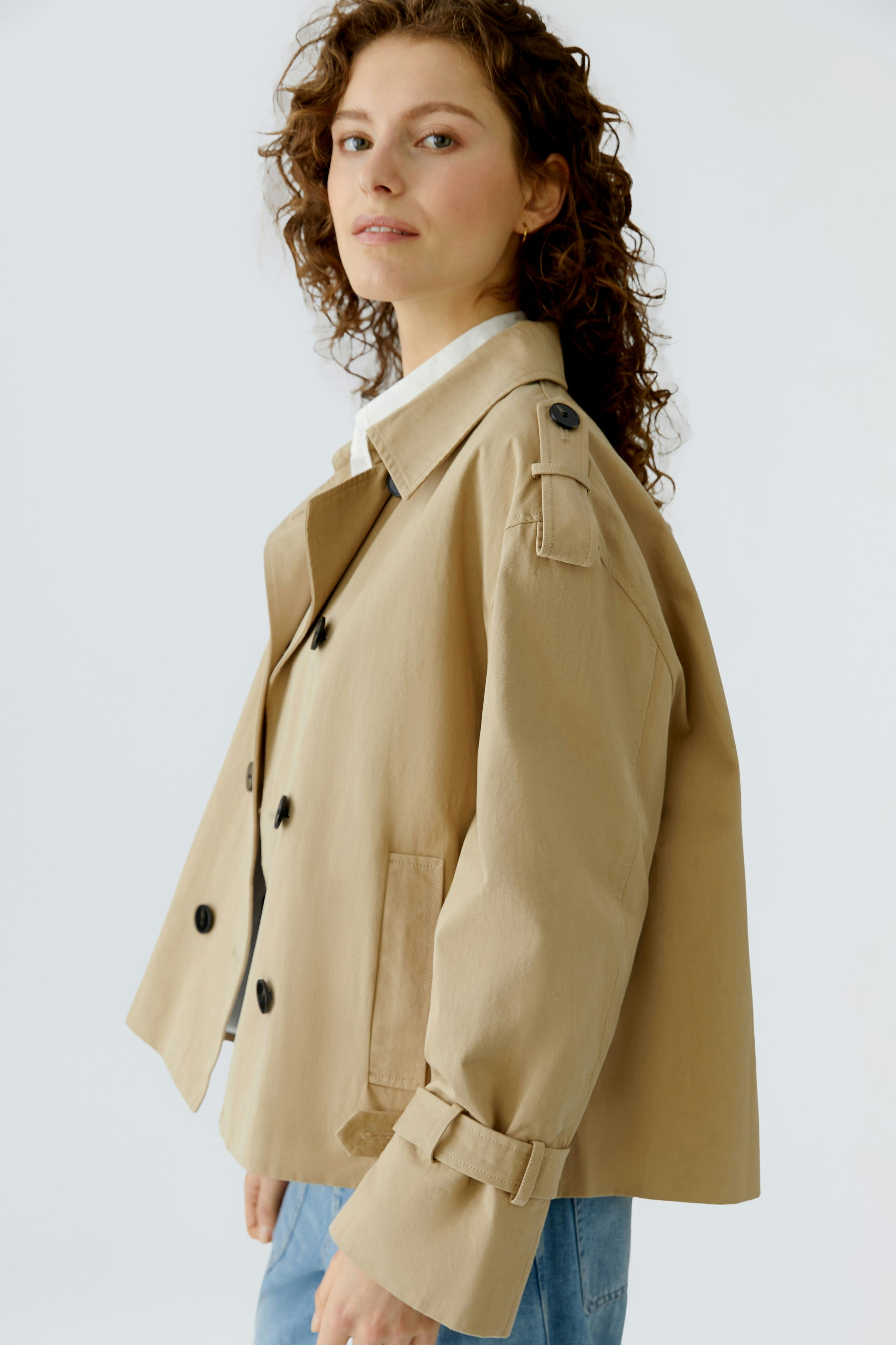 Casual women's jacket: A woman in a beige jacket with buttons and rolled sleeves poses confidently.
