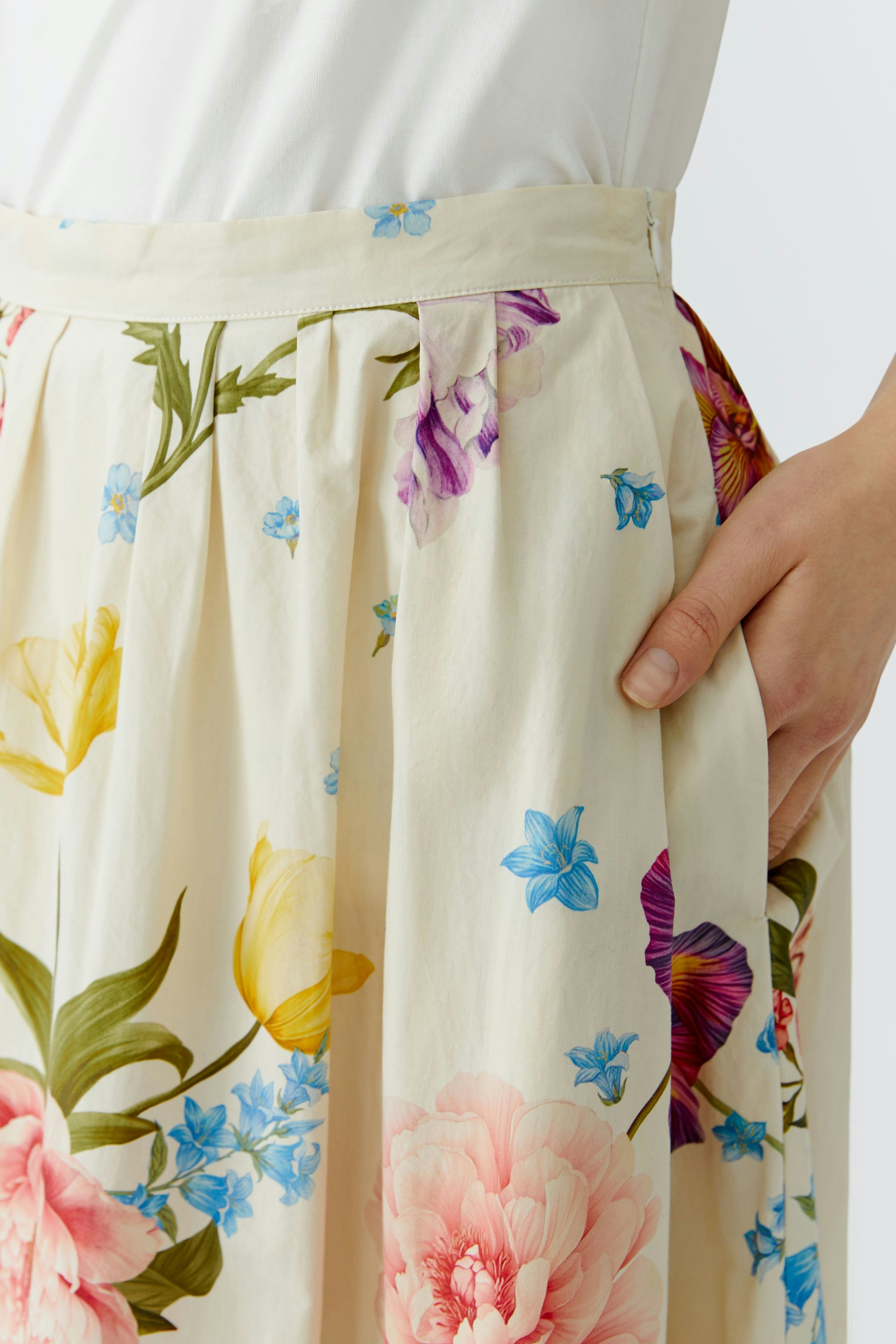 Floral midirock: Woman in a cream skirt with colorful flowers, showcasing a relaxed and vibrant style.