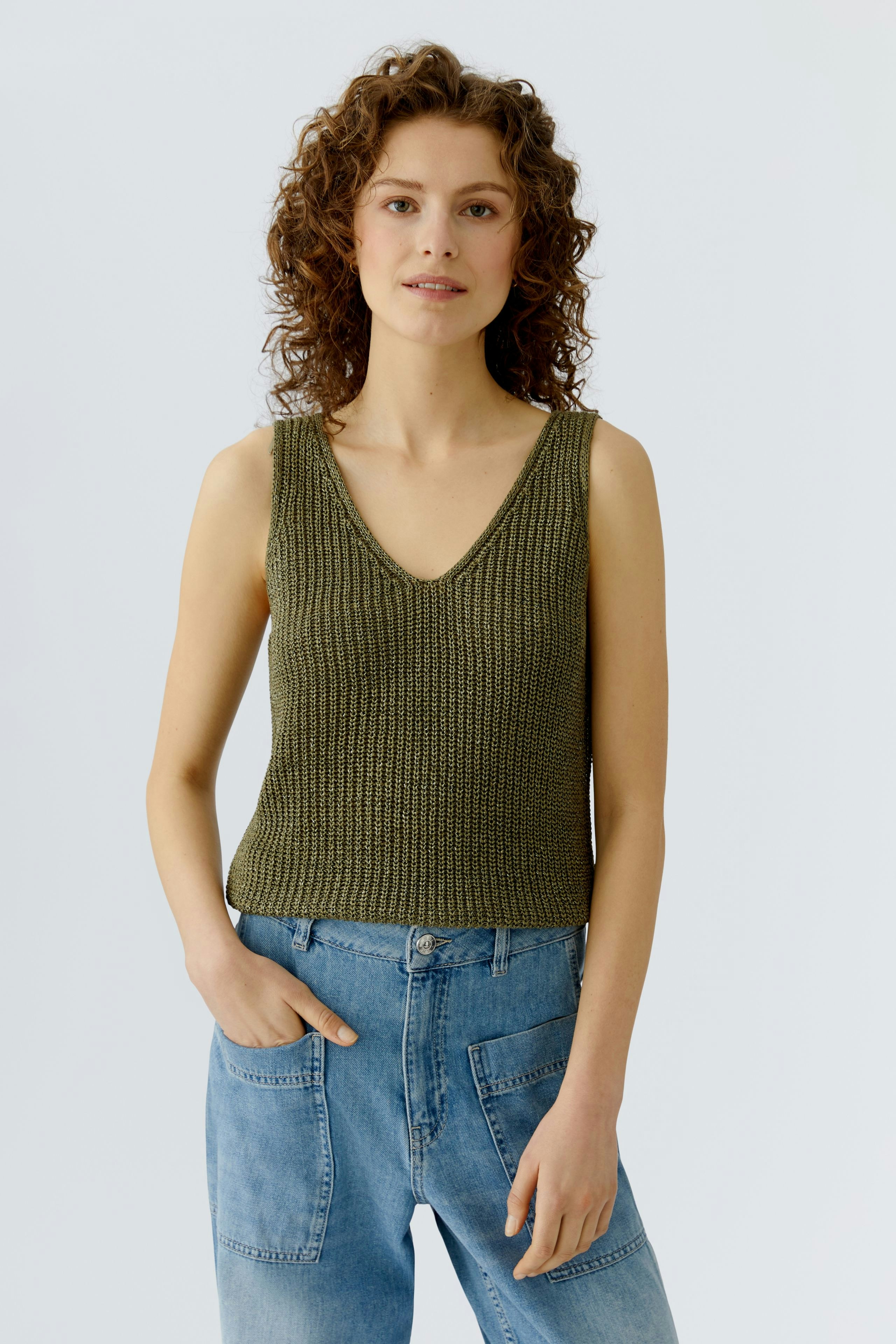 Casual women's top: A woman in a green knitted tank top paired with relaxed denim jeans.