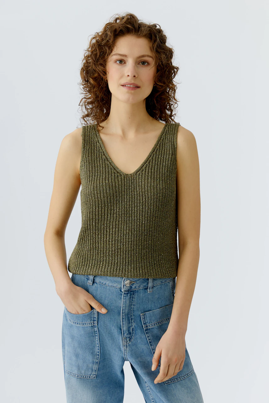 Casual women's top: A woman in a green knitted tank top paired with relaxed denim jeans.