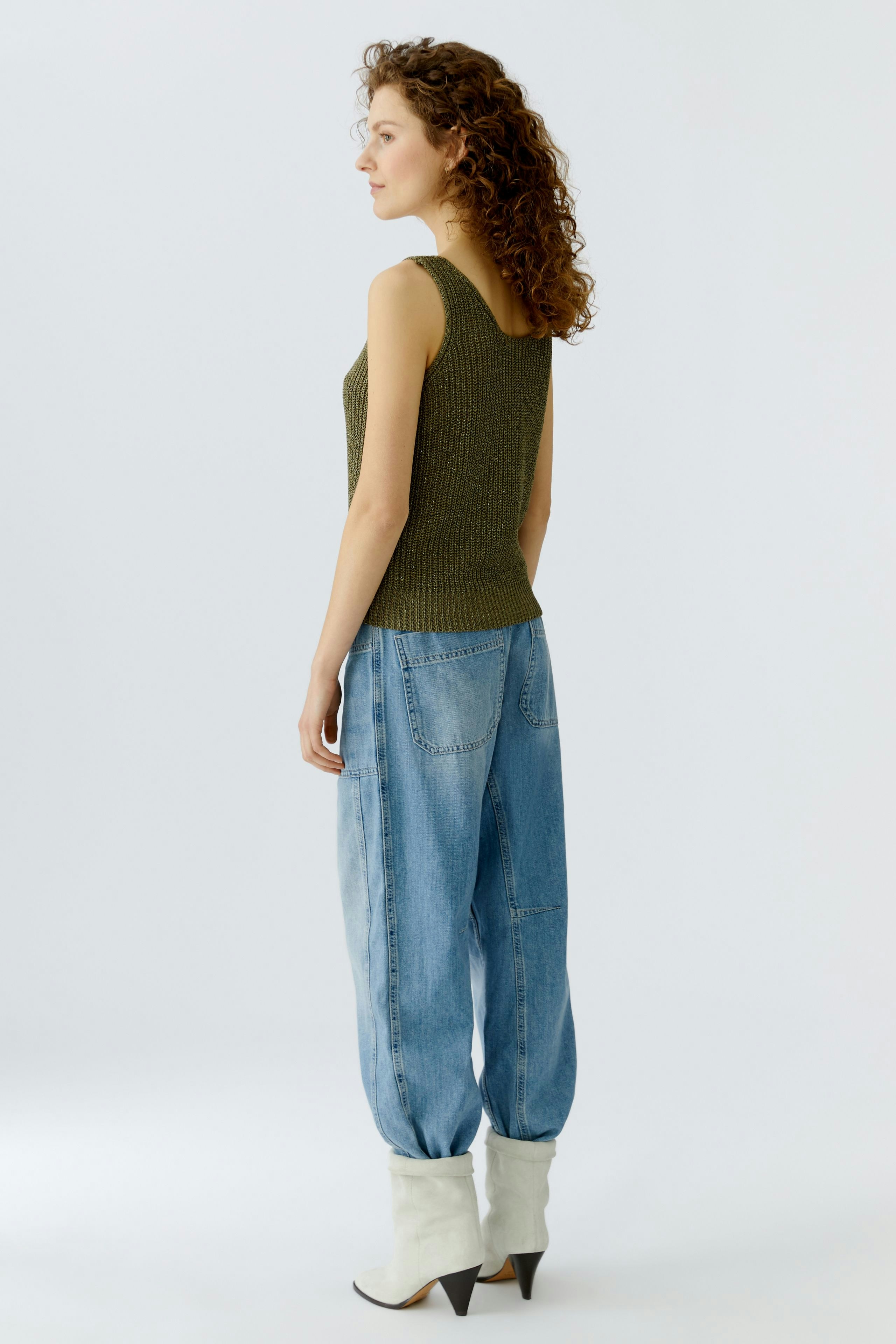 Casual women's top: A woman in a green sleeveless top and relaxed jeans stands confidently.