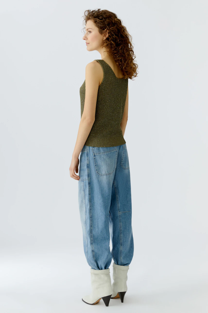 Casual women's top: A woman in a green sleeveless top and relaxed jeans stands confidently.