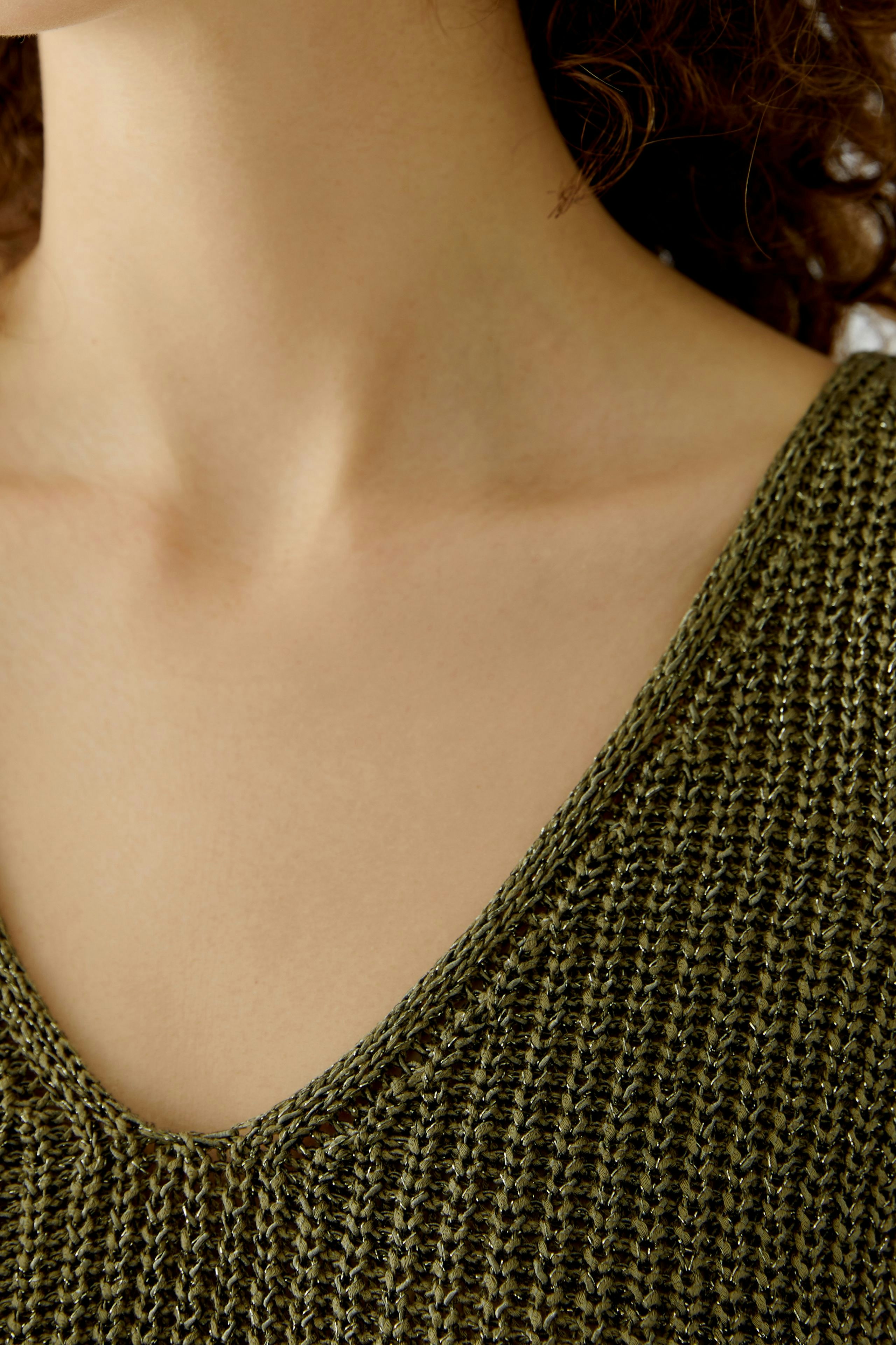 Casual women's top: Close-up of a woman wearing a green knitted top with a V-neck design.