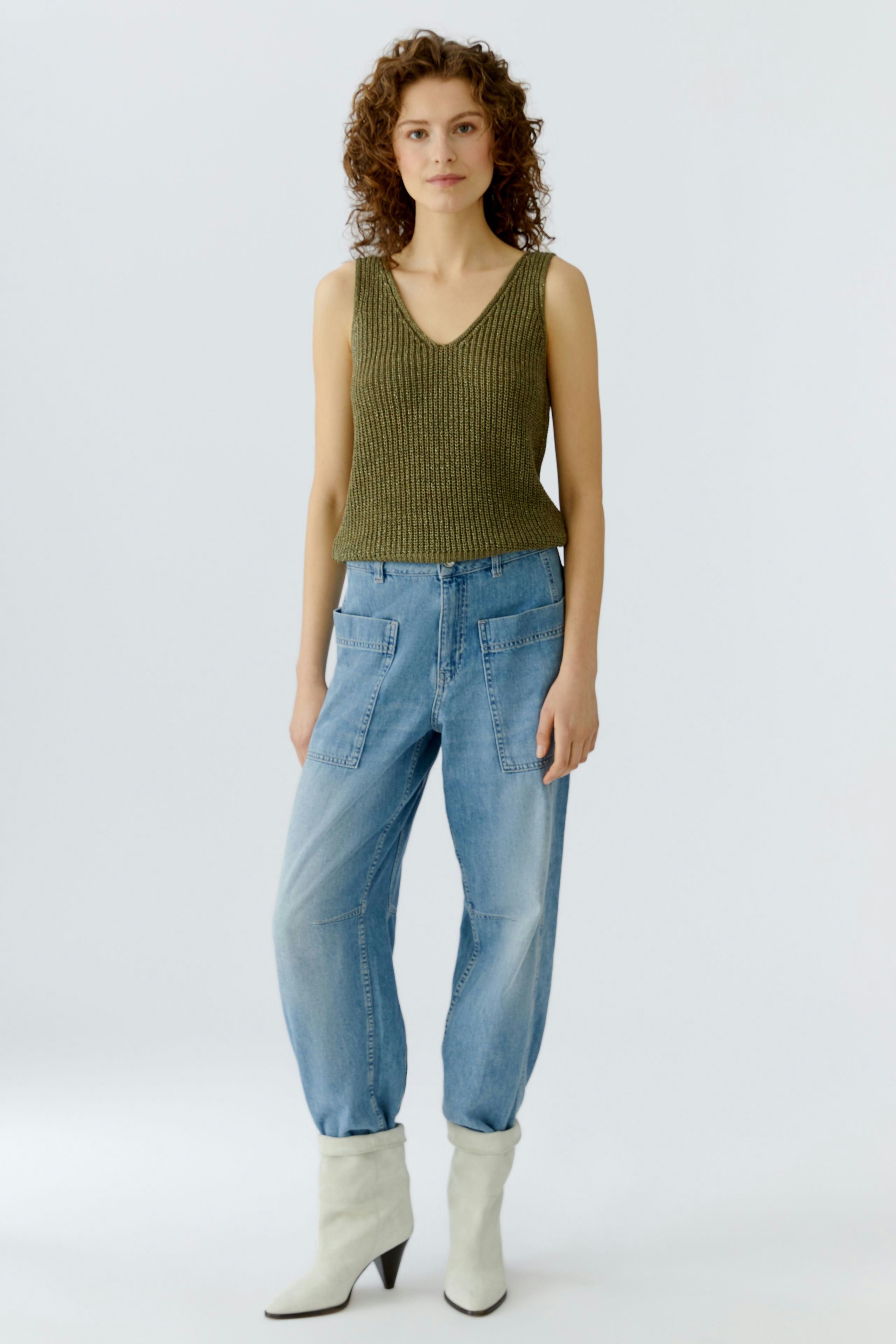 Casual women's top: A woman in a green knitted tank top paired with relaxed-fit jeans.