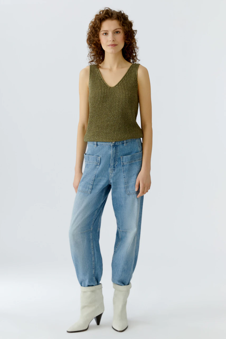 Casual women's top: A woman in a green knitted tank top paired with relaxed-fit jeans.