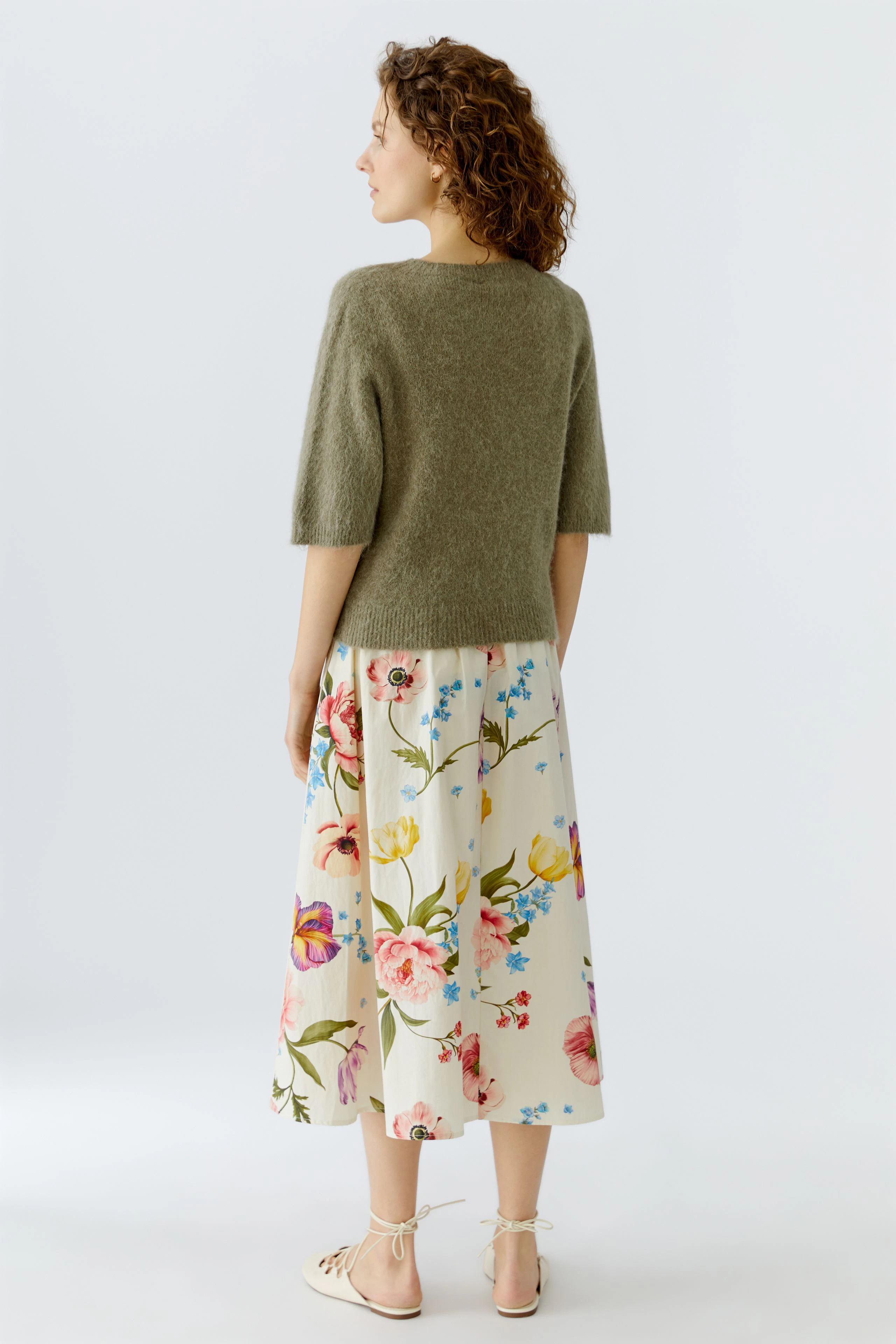 Damen-Pullover: Frau mit kurzem, grünem Strickpullover und floralem Rock von hinten.