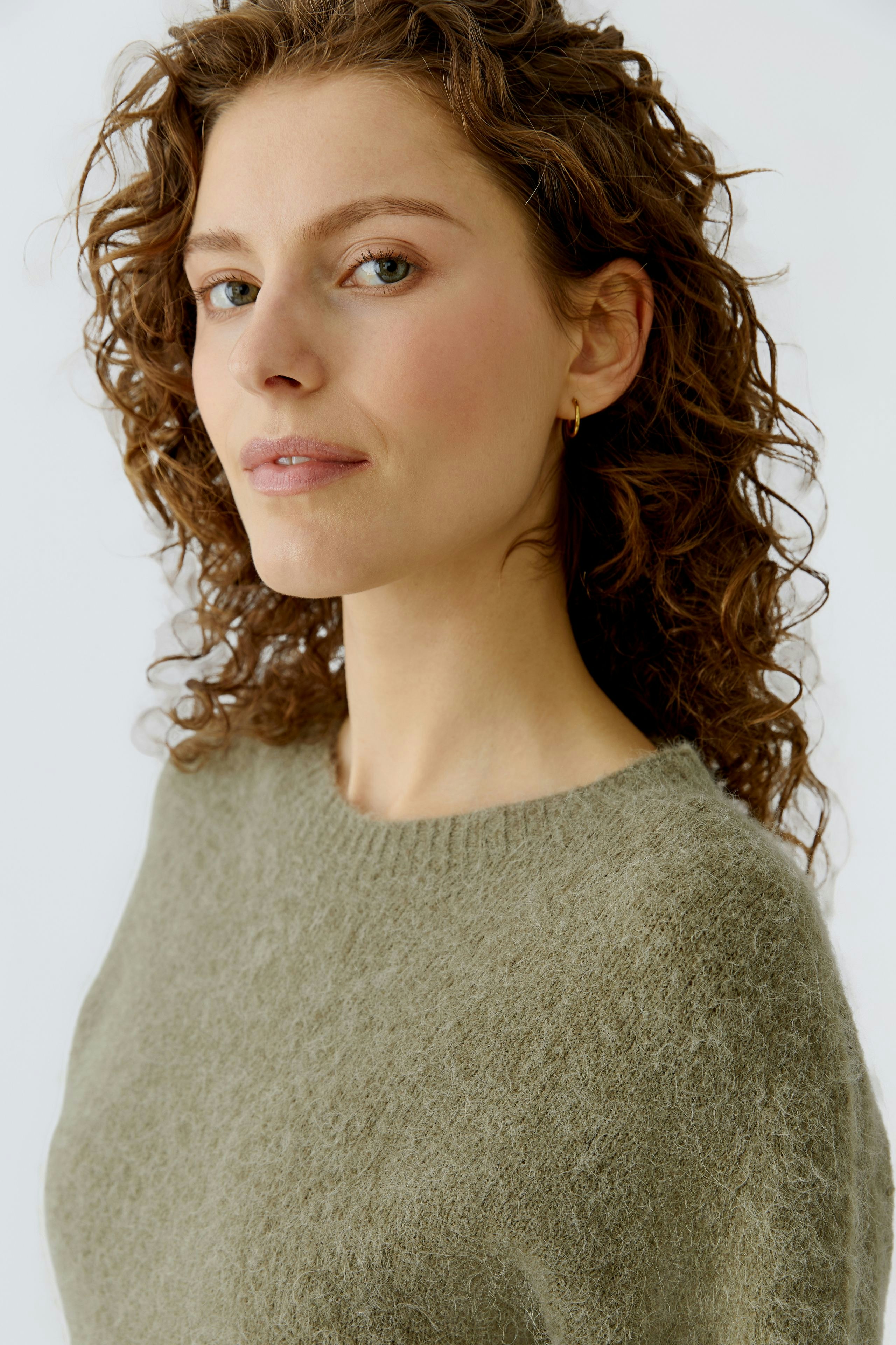 Casual women's pullover: A woman with curly hair wears a soft green pullover, looking confidently at the camera.