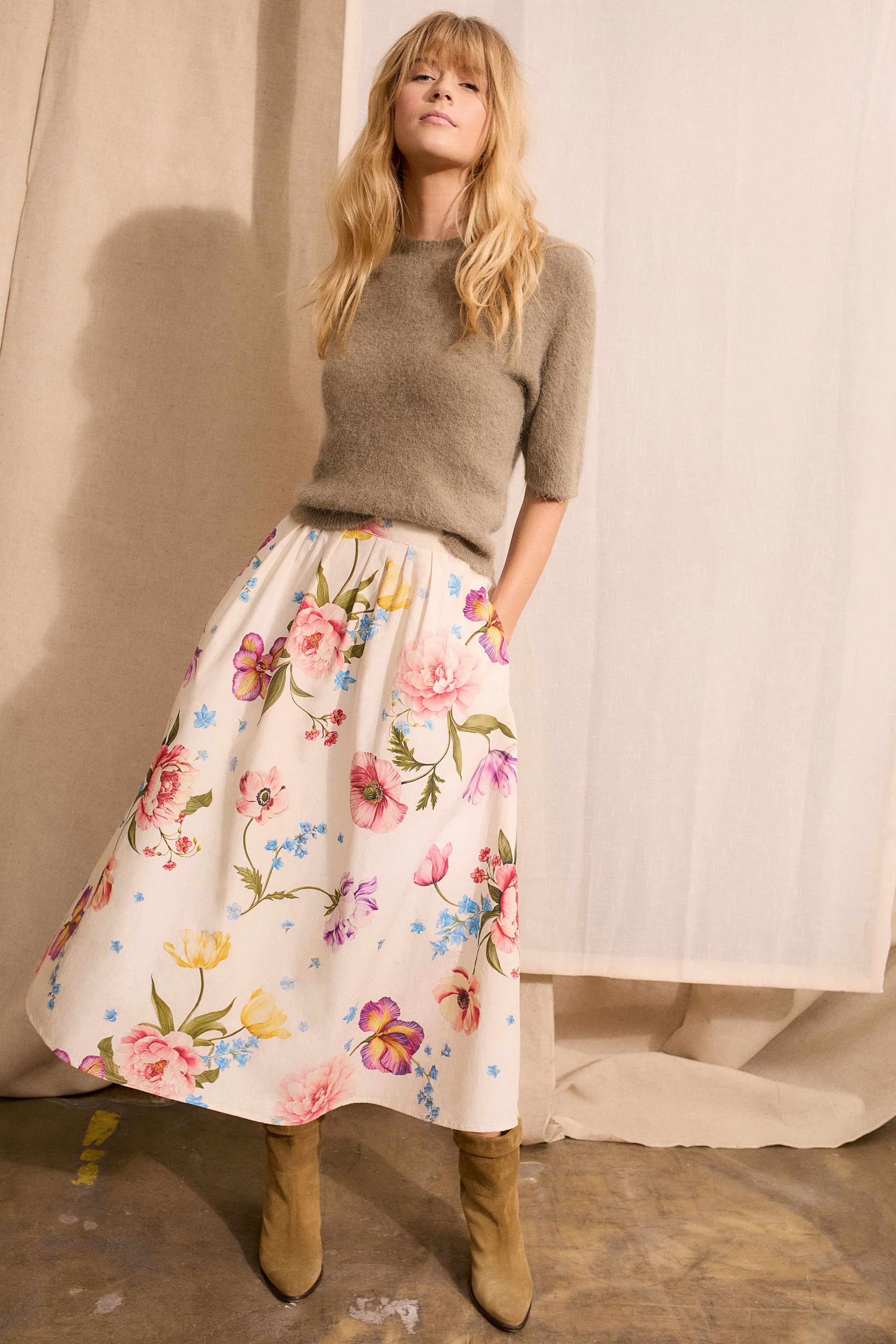 Damen-Pullover: Frau in grauem, kurzärmligem Pullover mit floralem Rock und Stiefeln.