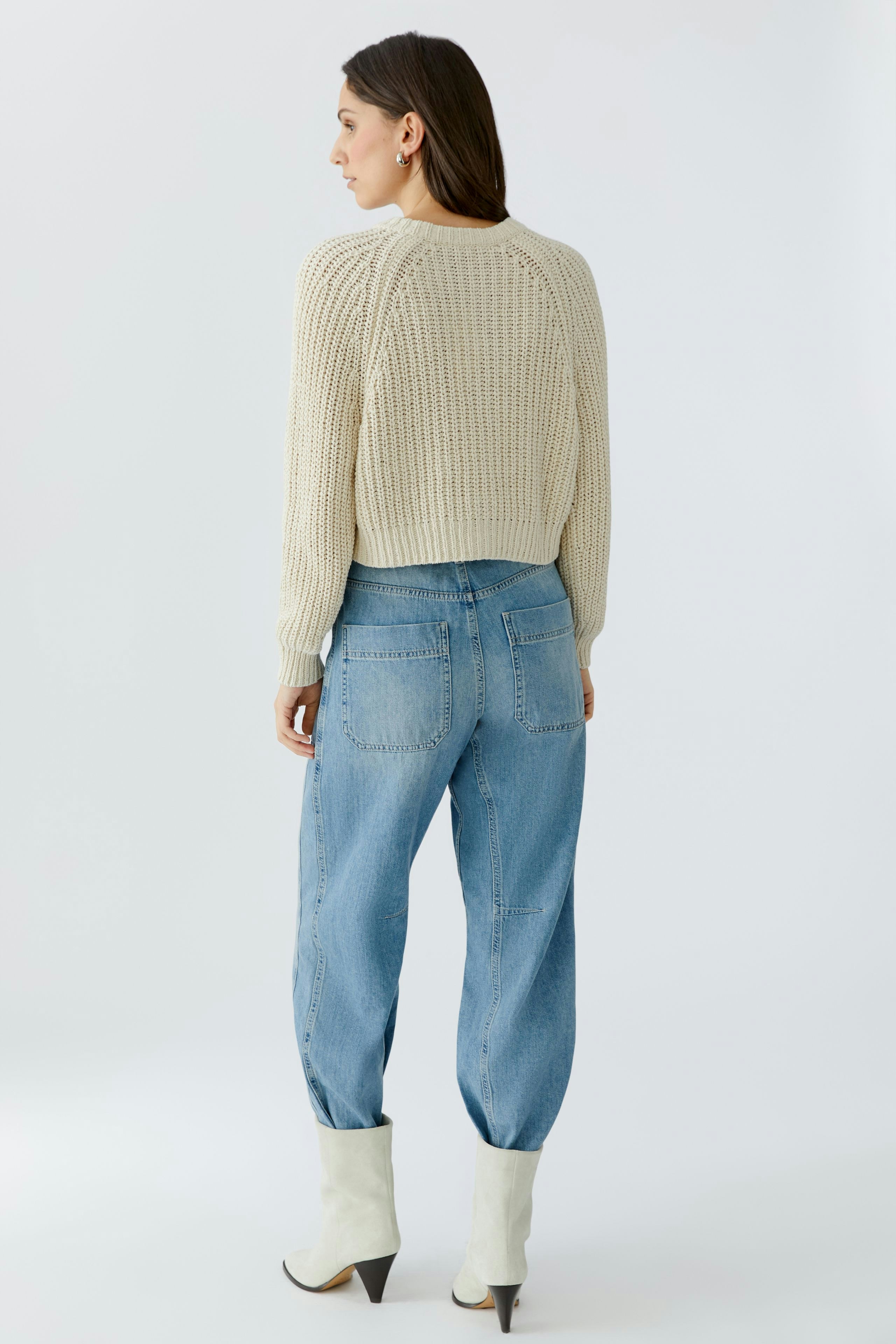 Casual women's cardigan: A woman in a light beige knitted cardigan paired with relaxed jeans.