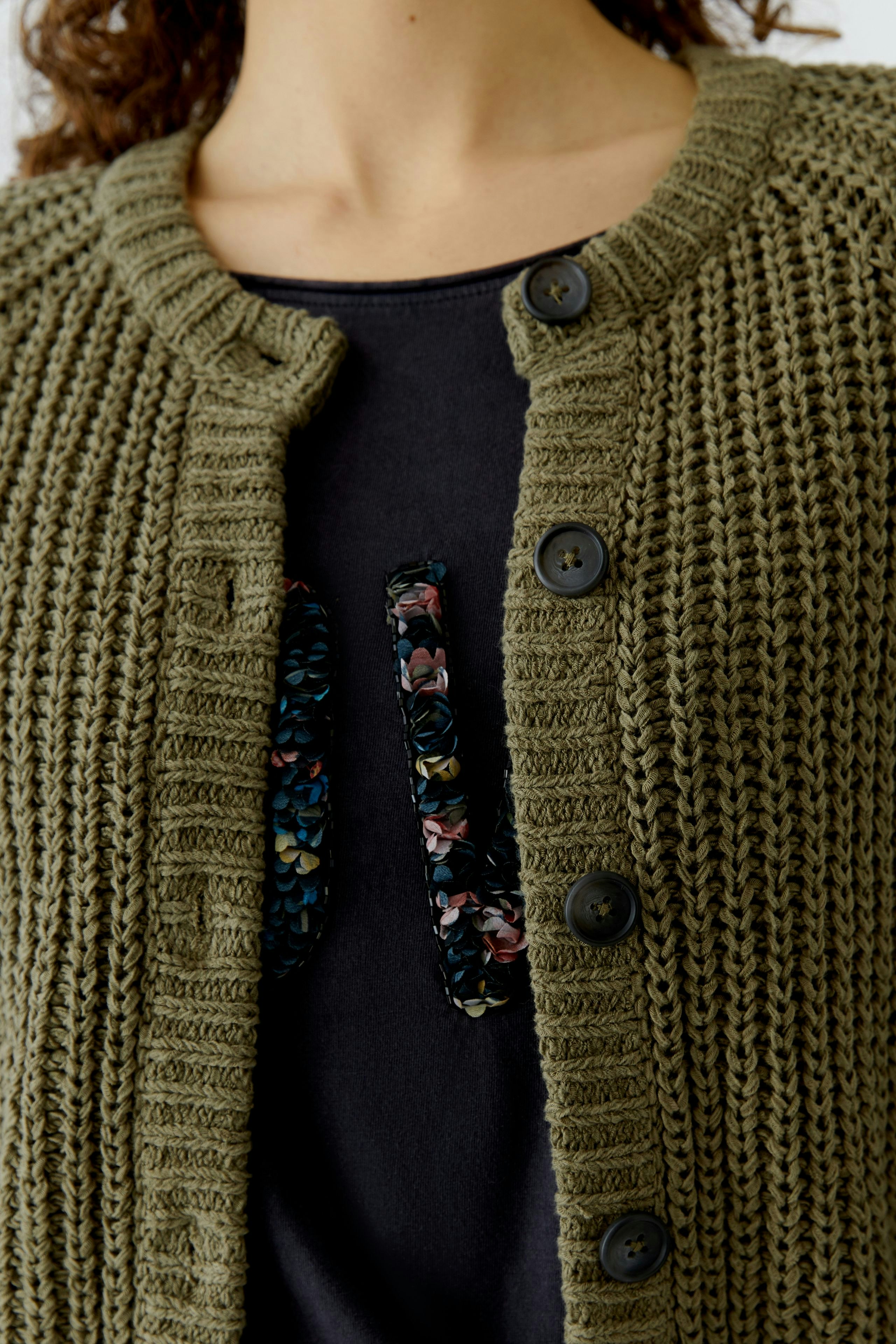 Casual women's cardigan: Close-up of a woman in an olive green knitted cardigan with buttons.