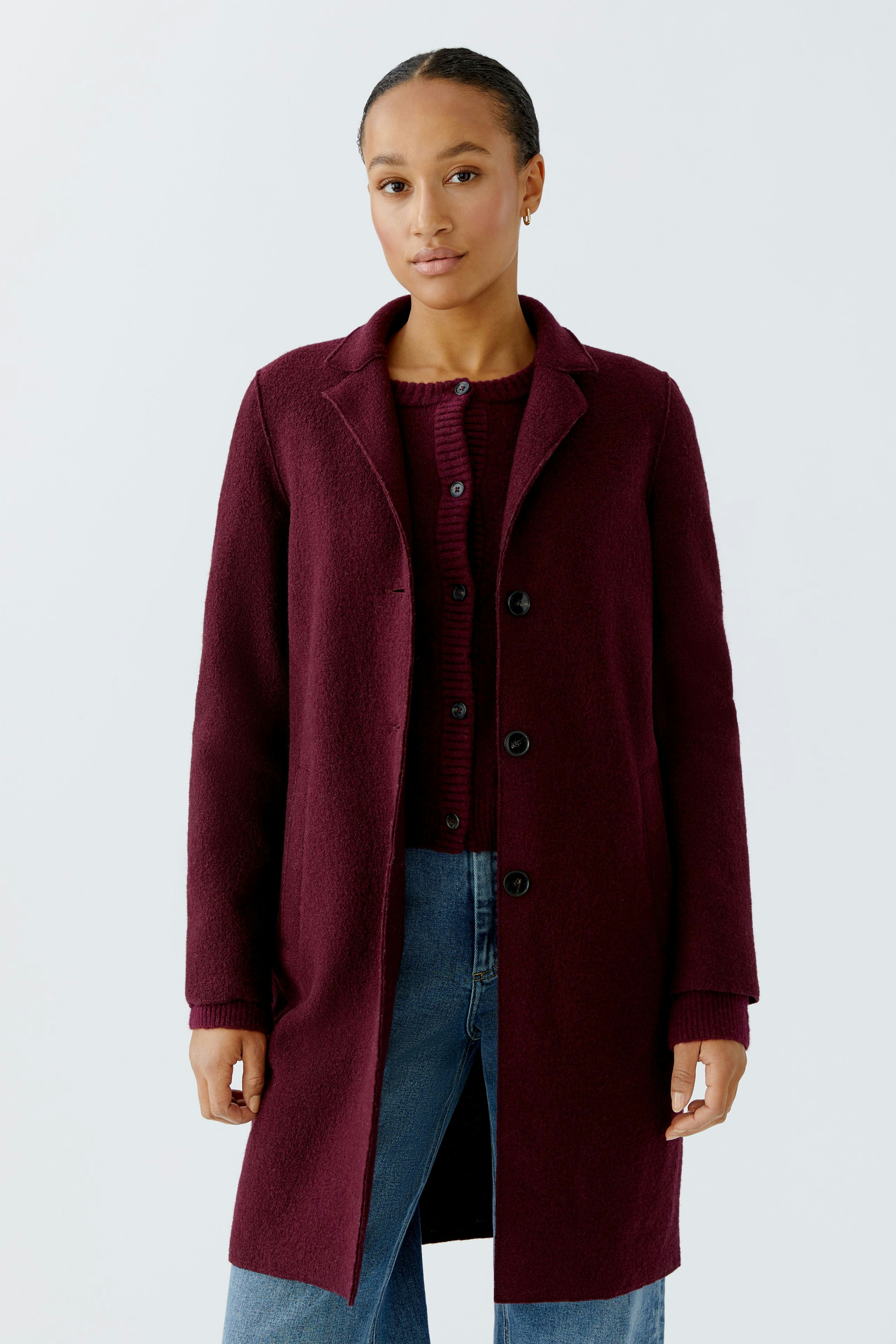 Modern women's wool coat: A woman in a burgundy coat over a red sweater and jeans stands confidently.