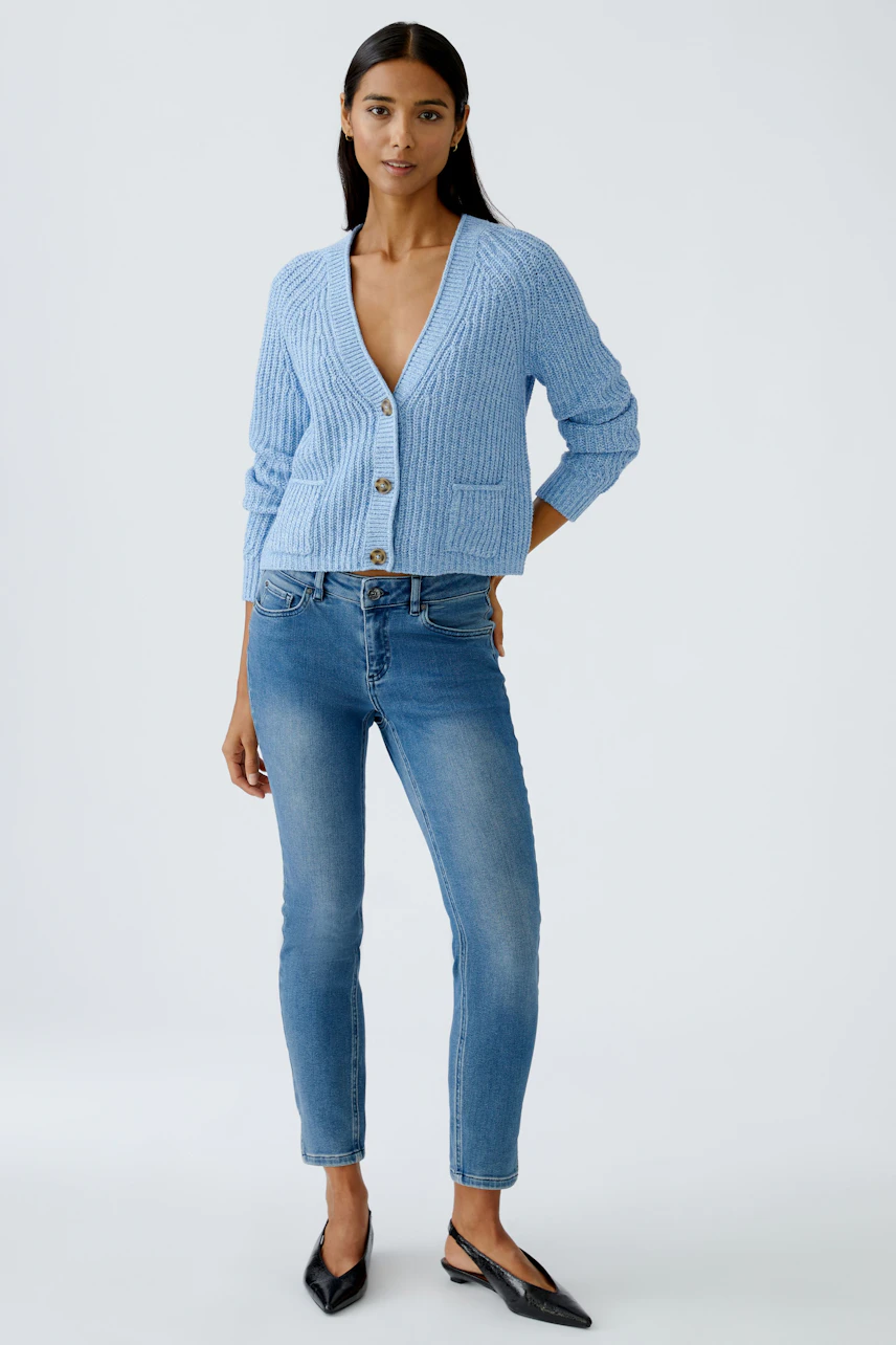 Stylish women's cardigan: A woman in a light blue cardigan with pockets and buttons, paired with white pants.
