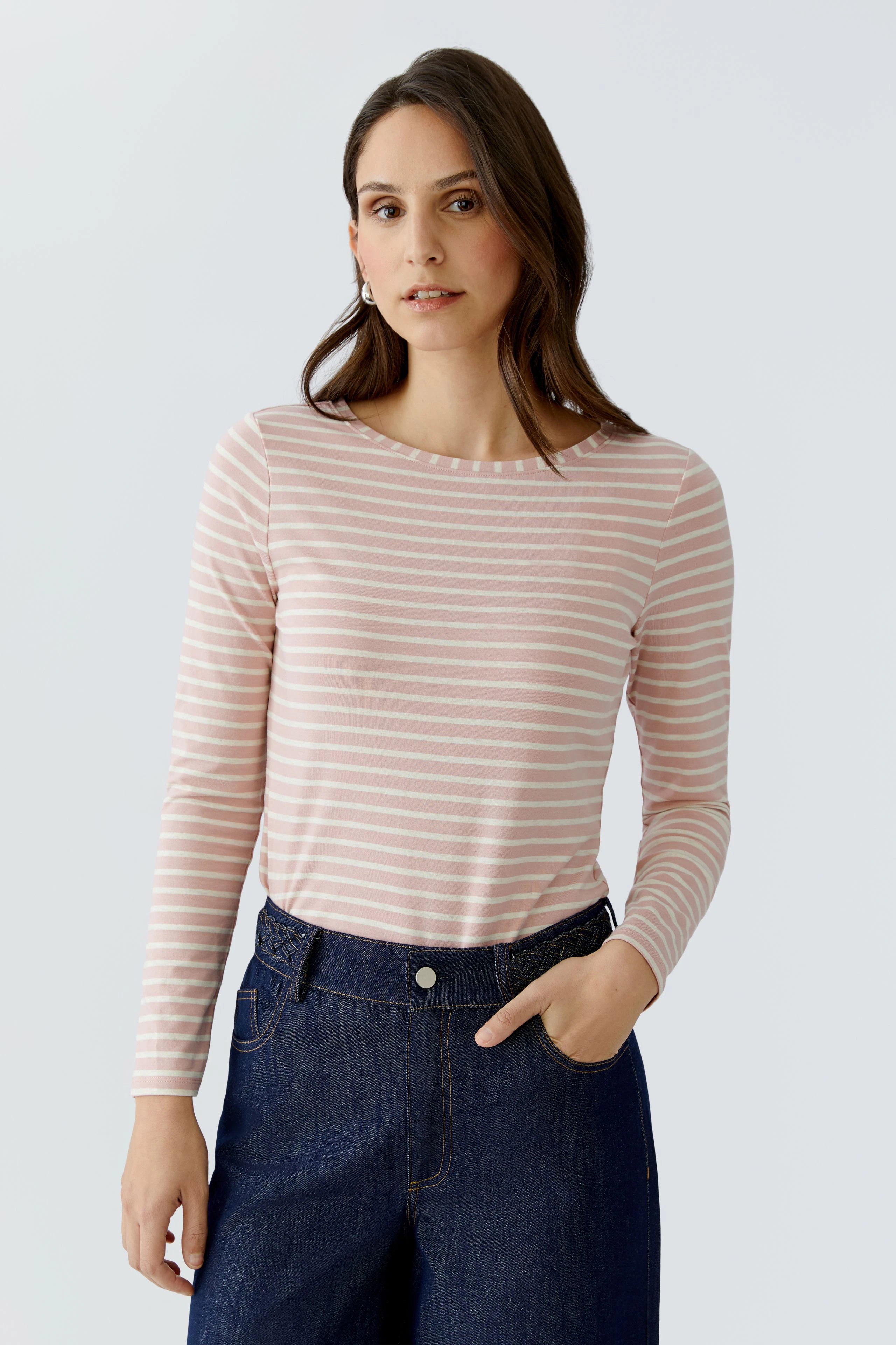 Casual long-sleeve shirt: Woman in a pink striped shirt paired with dark jeans, looking relaxed.