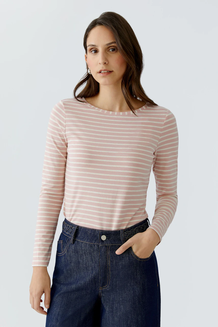 Casual long-sleeve shirt: Woman in a pink striped shirt paired with dark jeans, looking relaxed.
