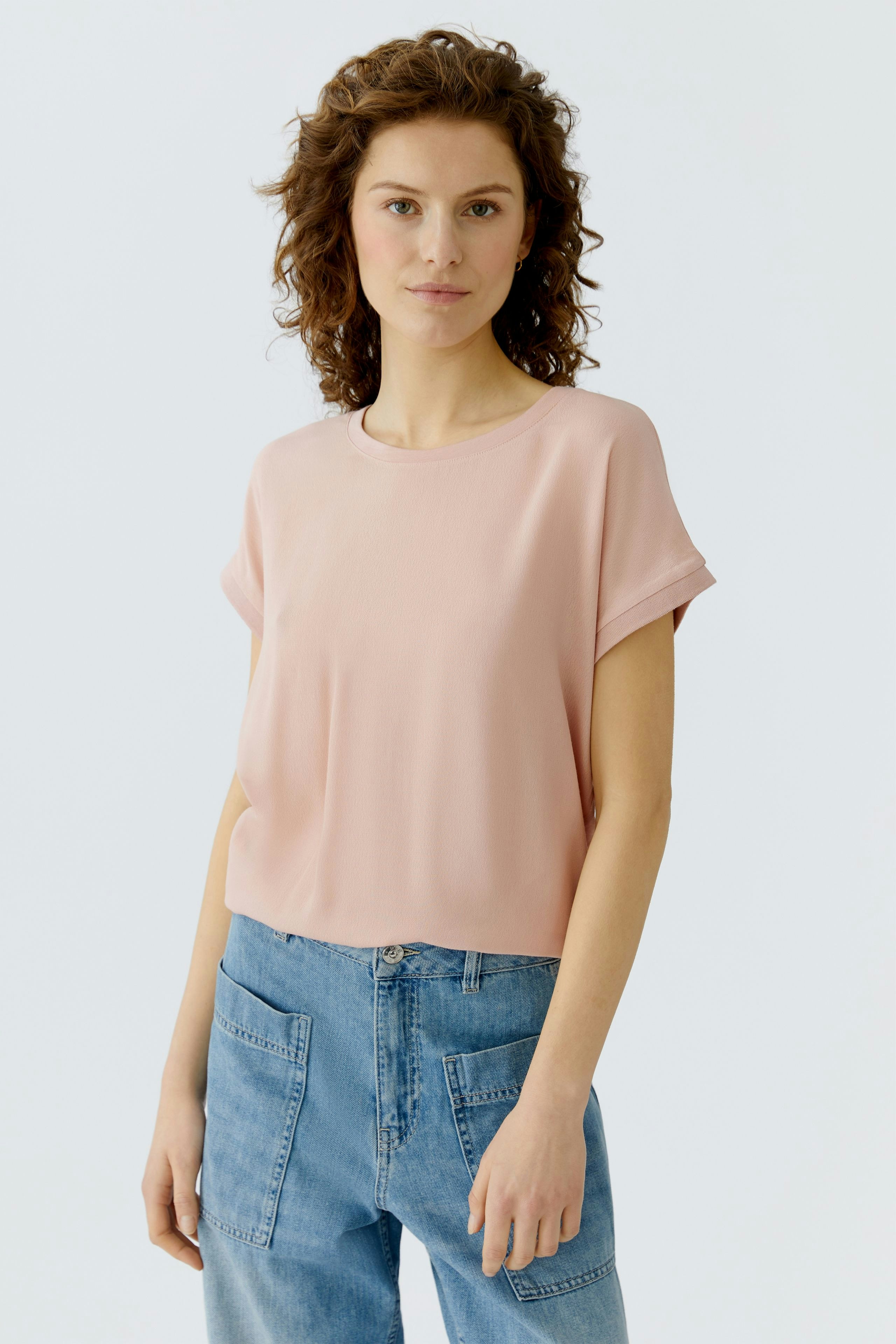 Casual women's blouse shirt: Woman in a light pink top with rolled sleeves and relaxed fit.