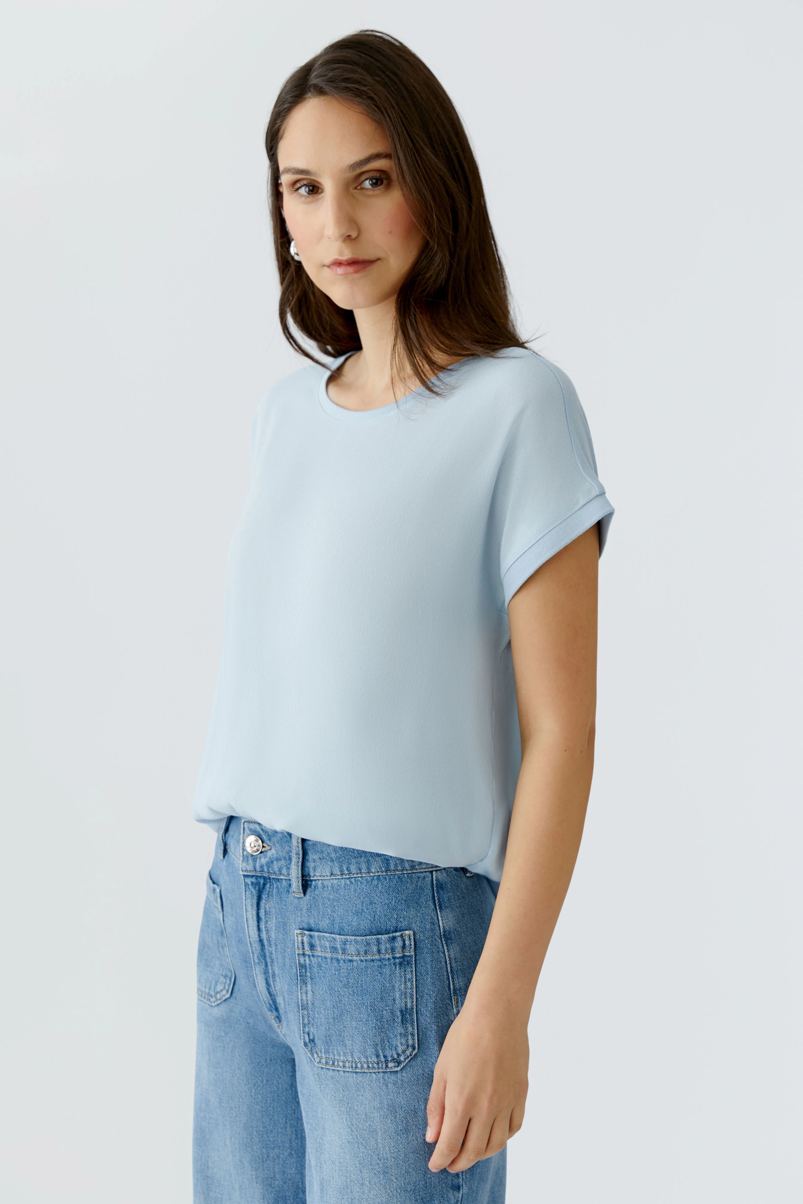 Luftiges Blusenshirt: Frau in hellblauem Shirt mit umgeschlagenen Ärmeln und lässigen Jeans.