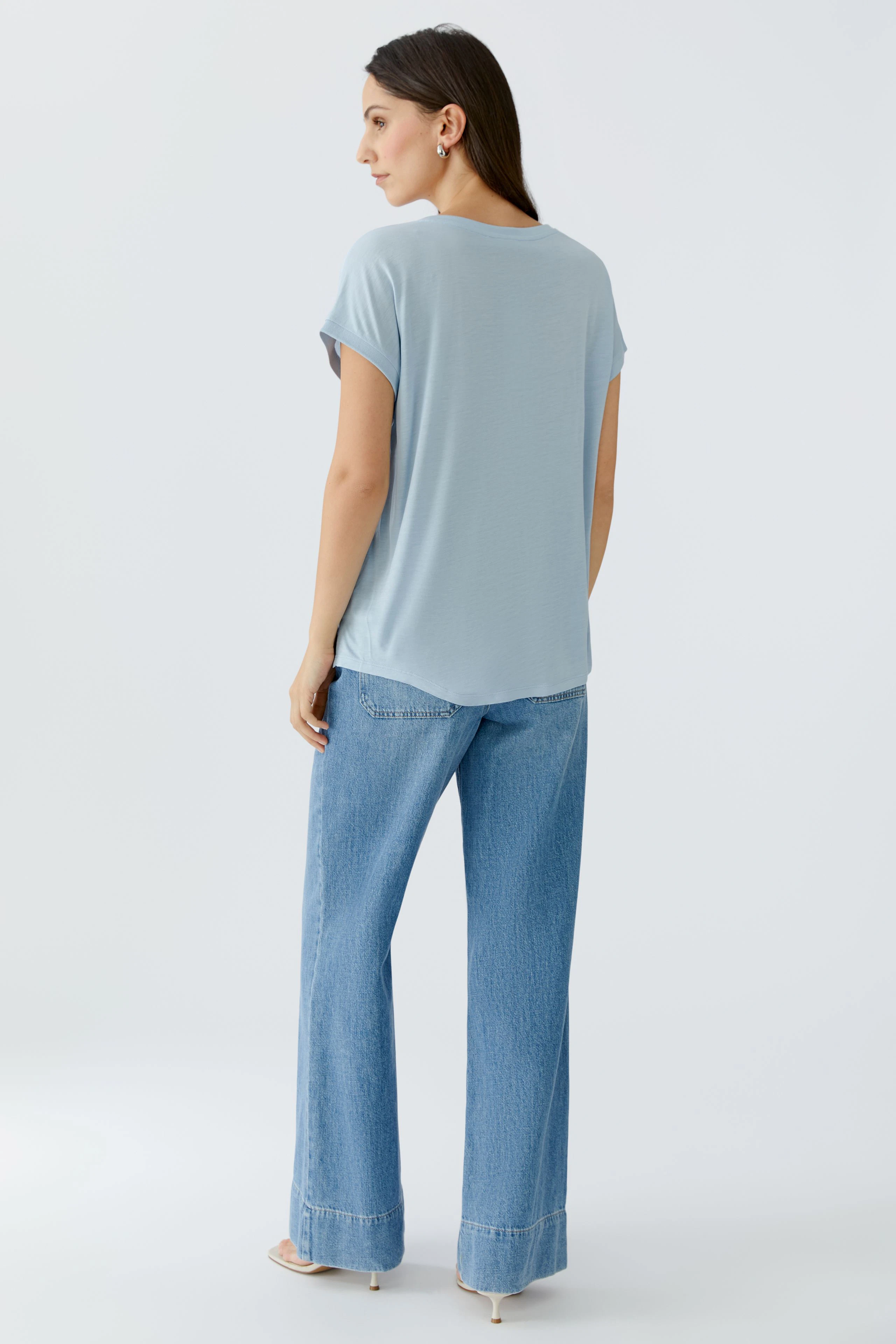 Bequemes Blusenshirt: Frau in hellblauem Shirt mit lässigen Jeans, von hinten betrachtet.