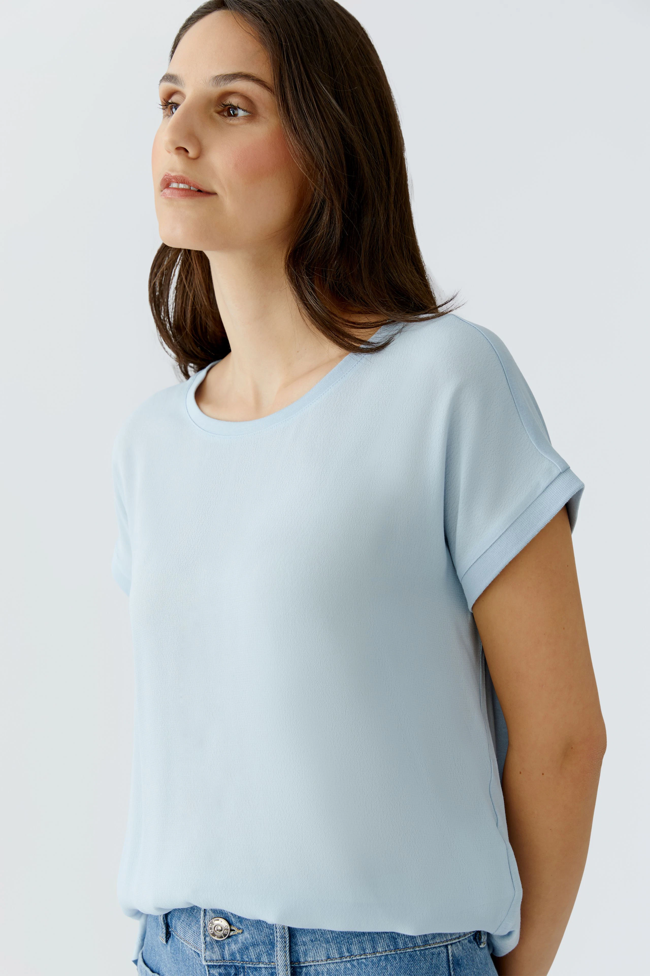 Leichtes Blusenshirt: Frau trägt ein hellblaues Shirt mit lässigem Schnitt und umgeschlagenen Ärmeln.