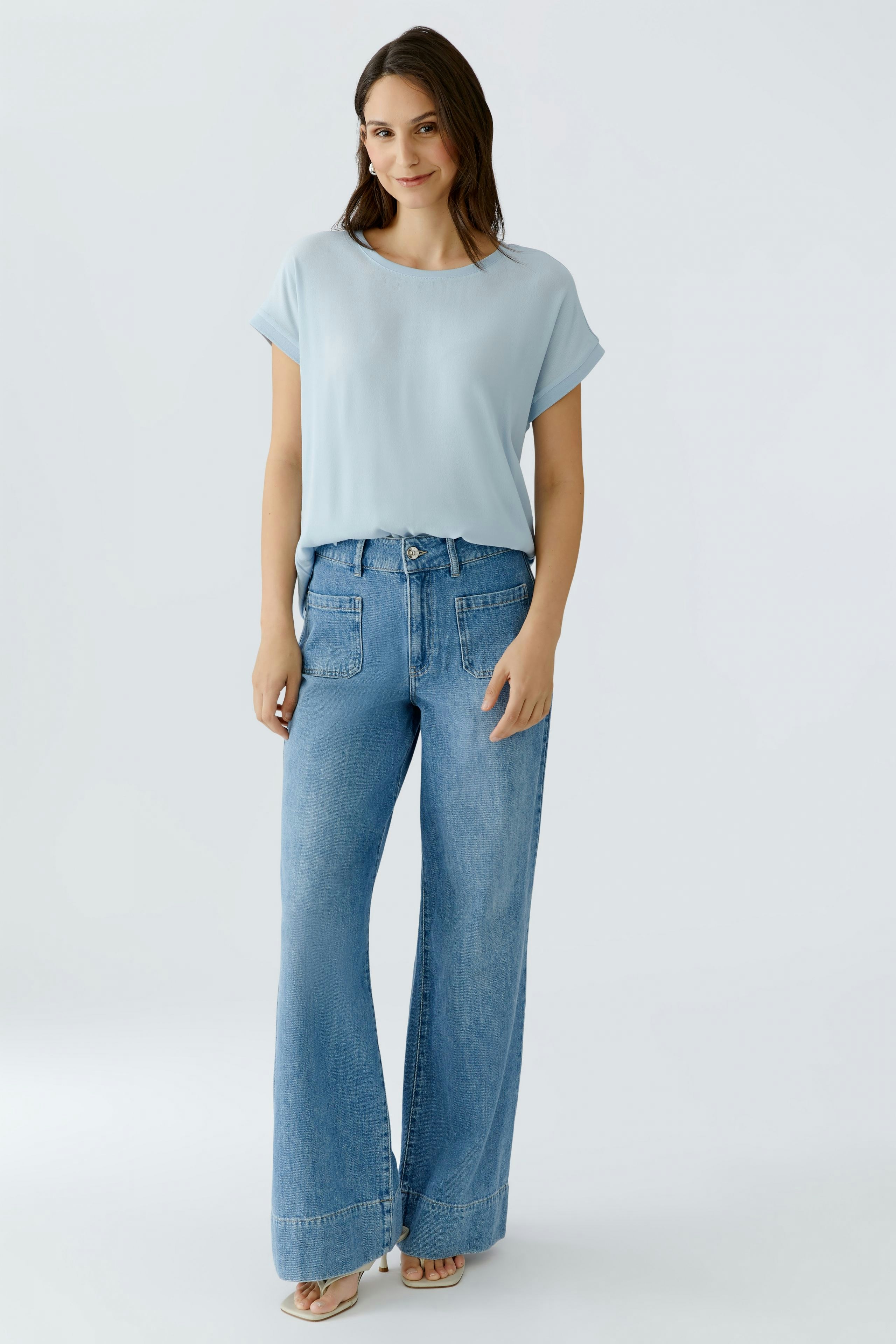 Luftiges Blusenshirt: Frau trägt ein hellblaues, lässiges Blusenshirt mit umgeschlagenen Ärmeln.