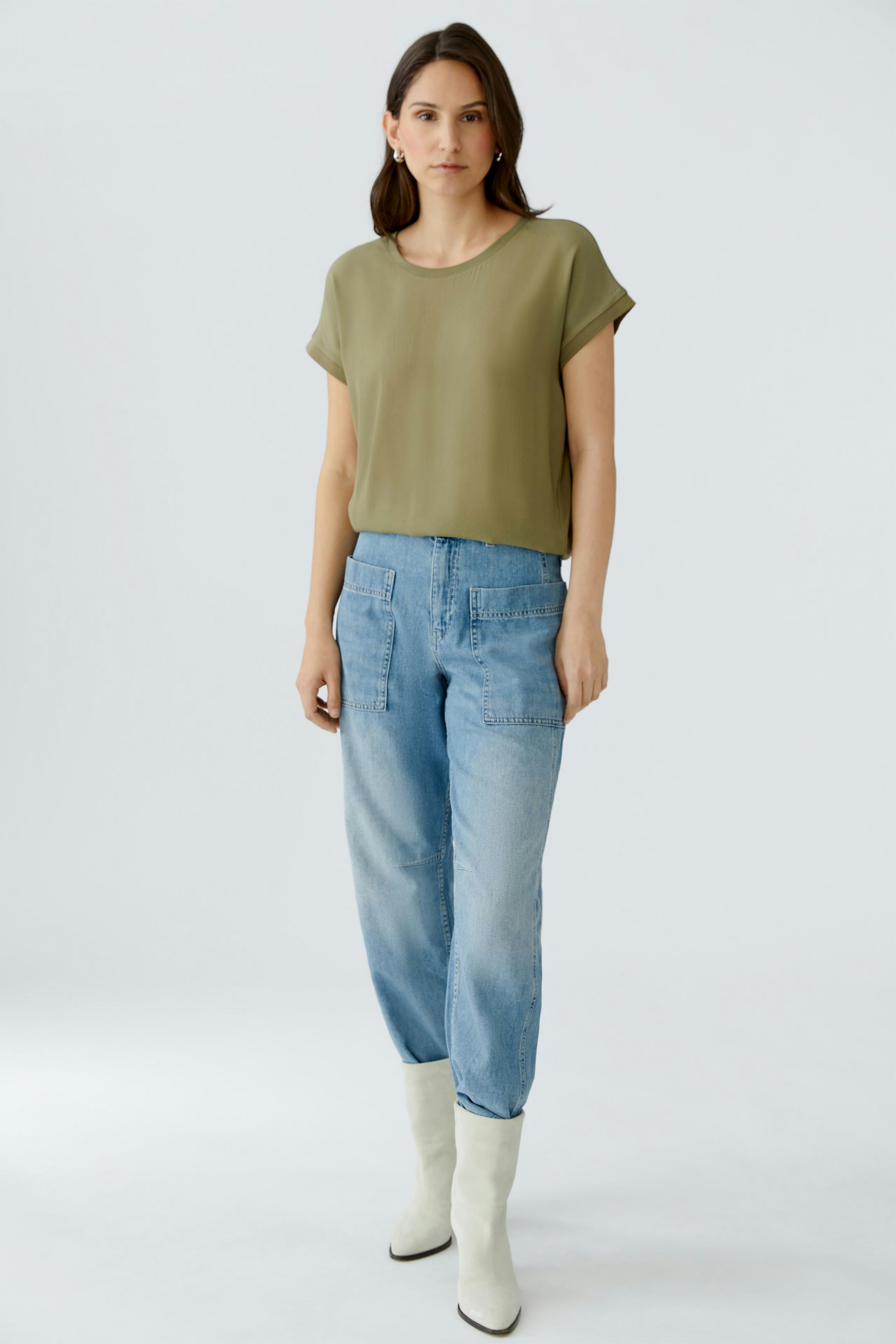Casual women's blouse shirt: Woman in a loose olive green top paired with light blue jeans.