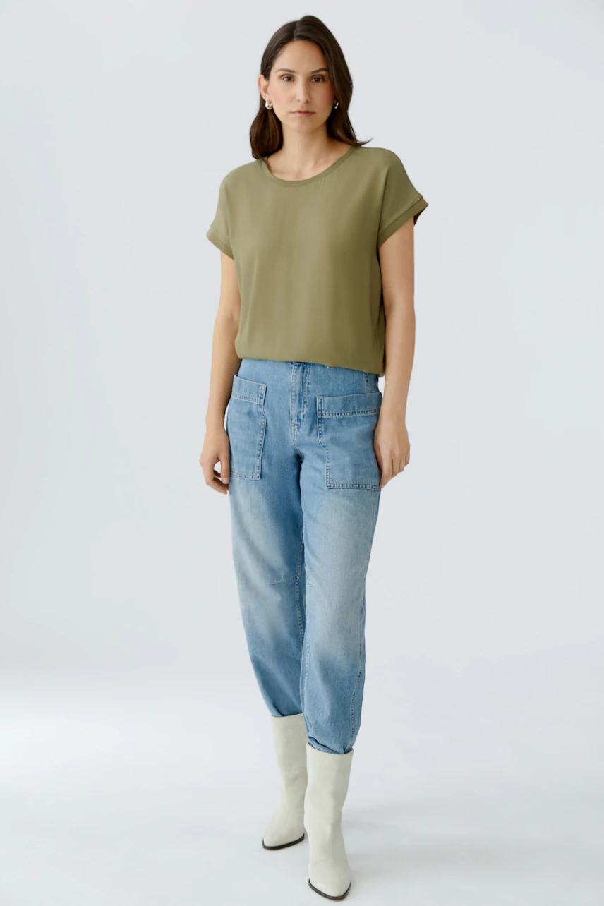 Casual women's blouse shirt: Woman in a loose olive green top paired with light blue jeans.